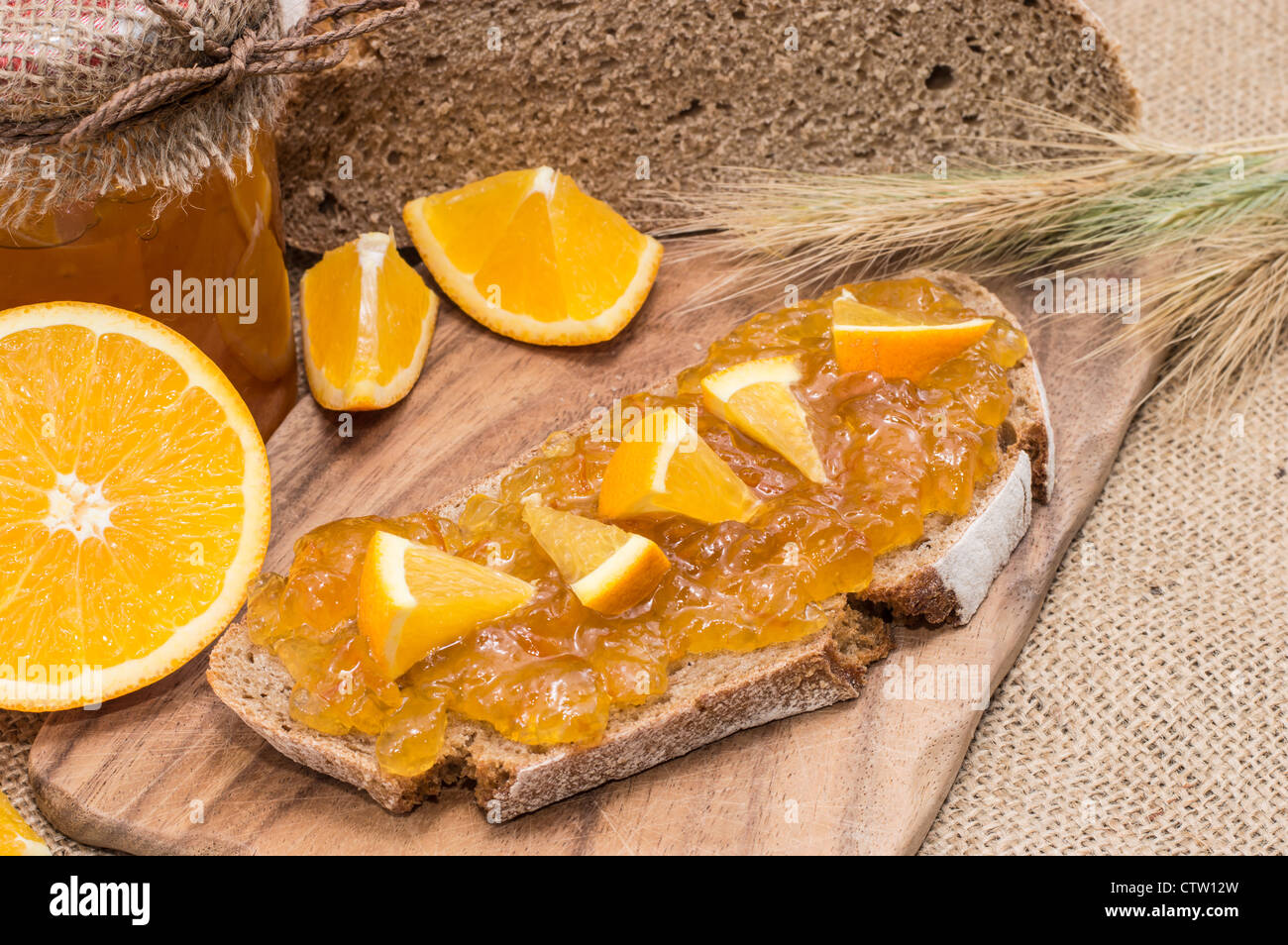 Pane con marmellata di arancio e frutta fresca su sfondo rustico Foto Stock