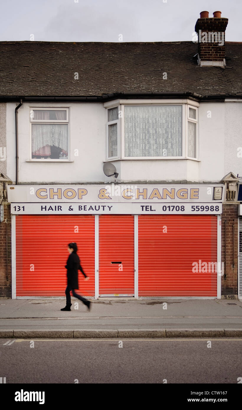 Una donna che cammina passato chiuso un salone di bellezza con persiane rosse in Rainham, Essex. Foto Stock