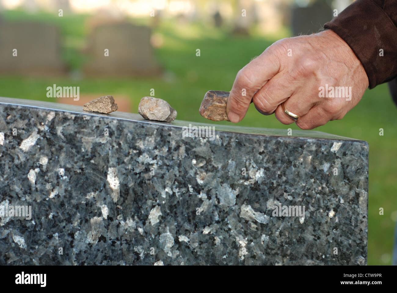 Mano d'uomo ponendo una pietra sulla cima di una lapide in un cimitero. Foto Stock