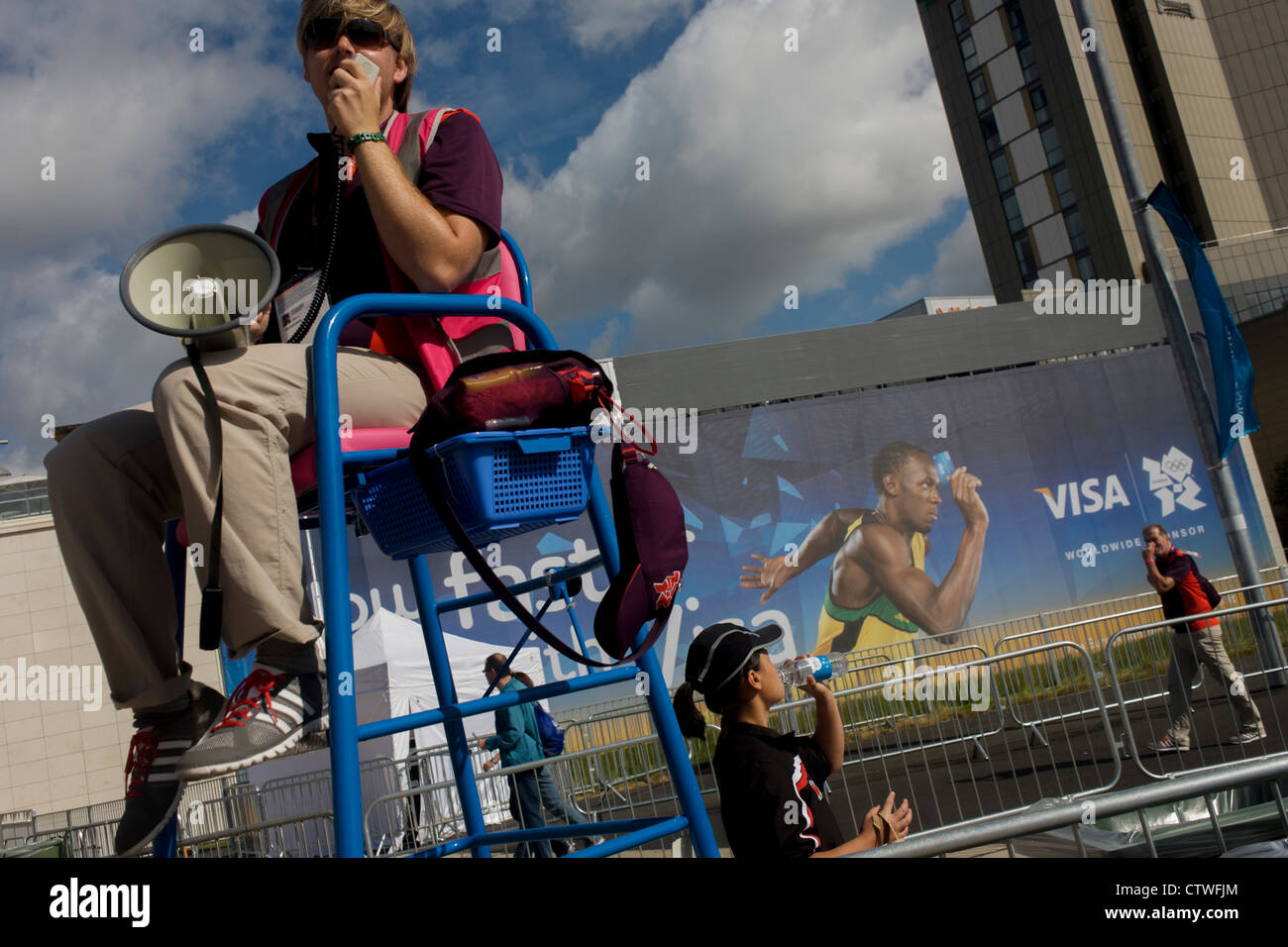 Un produttore di giochi volontario utilizza un megafono per intrattenere gli spettatori passando un Usain Bolt Visa billboard durante il London 2012 Olympic Park durante i giochi. Londra 2012 volontari sono chiamati 'Giochi Makers', come stanno contribuendo a rendere i giochi accadere. Fino a 70.000 giochi politici prendere su di una ampia varietà di ruoli attraverso le sedi: da accogliere i visitatori, per il trasporto di atleti; ad aiutare dietro le quinte nella tecnologia team per assicurarsi che i risultati visualizzare quanto più rapidamente e accuratamente possibile. Foto Stock