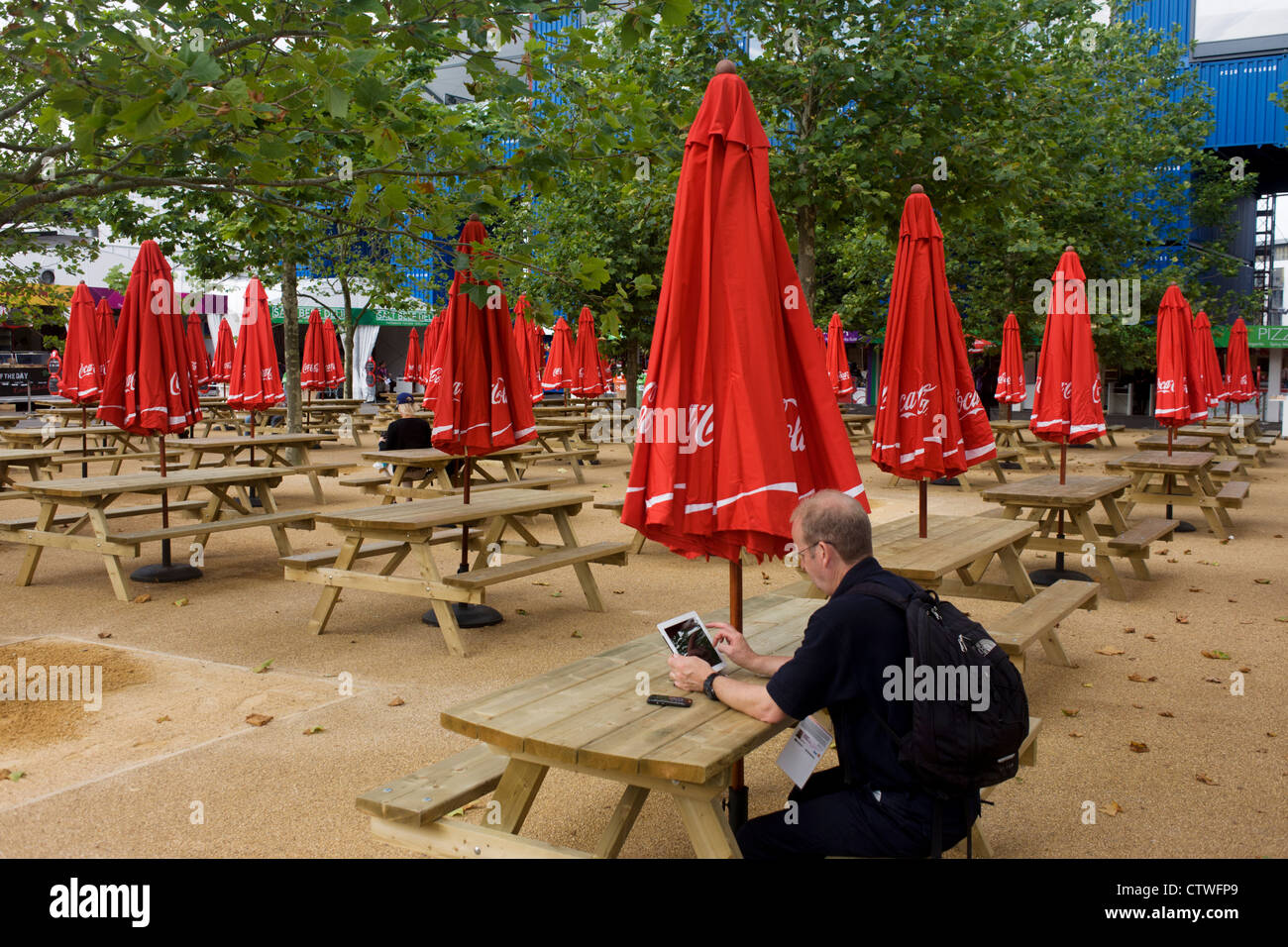 Uno spettatore utilizza un iPad per gli aggiornamenti dei risultati sotto la coca cola con marchio brolleys sponsor nel Parco Olimpico durante le Olimpiadi di Londra 2012. La Coca Cola Company ha sostenuto i Giochi Olimpici ha cominciato in 1928, ora a 92 anni associazione senza interruzione. Foto Stock