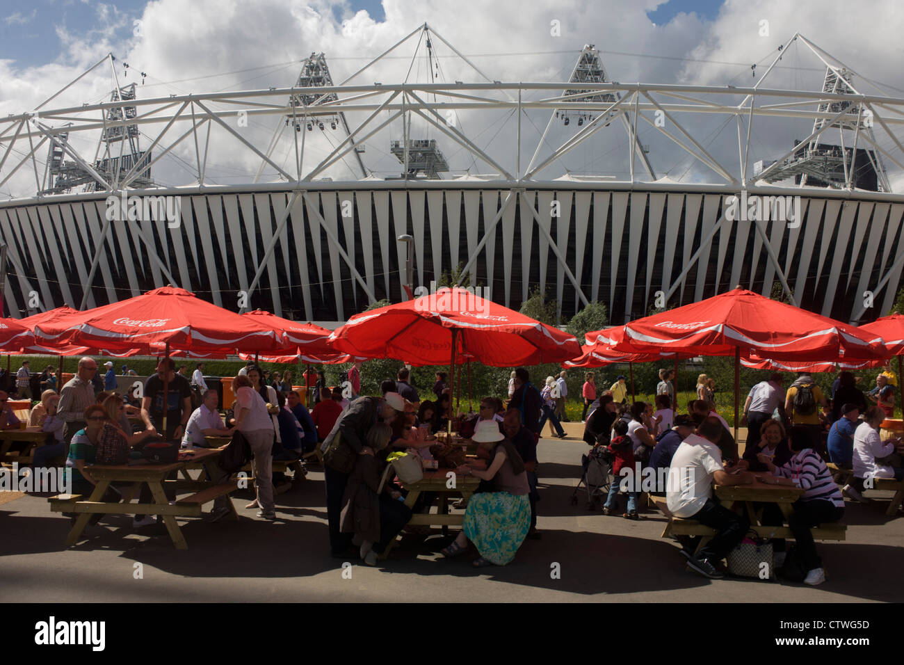 Spettatori mangiare sotto il marchio Coca-Cola sponsor brolleys nel vicino alla stadio principale nel Parco Olimpico durante le Olimpiadi di Londra 2012. La Coca Cola Company ha sostenuto i Giochi Olimpici ha cominciato in 1928, ora a 92 anni associazione senza interruzione. Questa terra è stata trasformata in un 2.5 sq km complesso sportivo, una volta che le imprese industriali ed ora sede di otto luoghi di interesse tra cui il principale arena, Aquatics Centre e Velodromo plus degli atleti del Villaggio Olimpico. Foto Stock