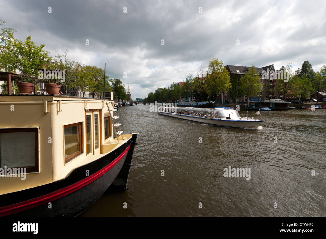 Houseboat in amsterdam canal con una gita in barca passando da Foto Stock