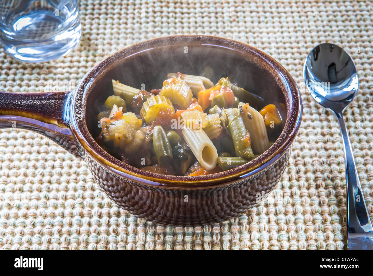 Recipiente di ceramica di stile italiano di zuppa di verdure su tessuto di cartellone con cucchiaio e bicchiere di acqua Foto Stock