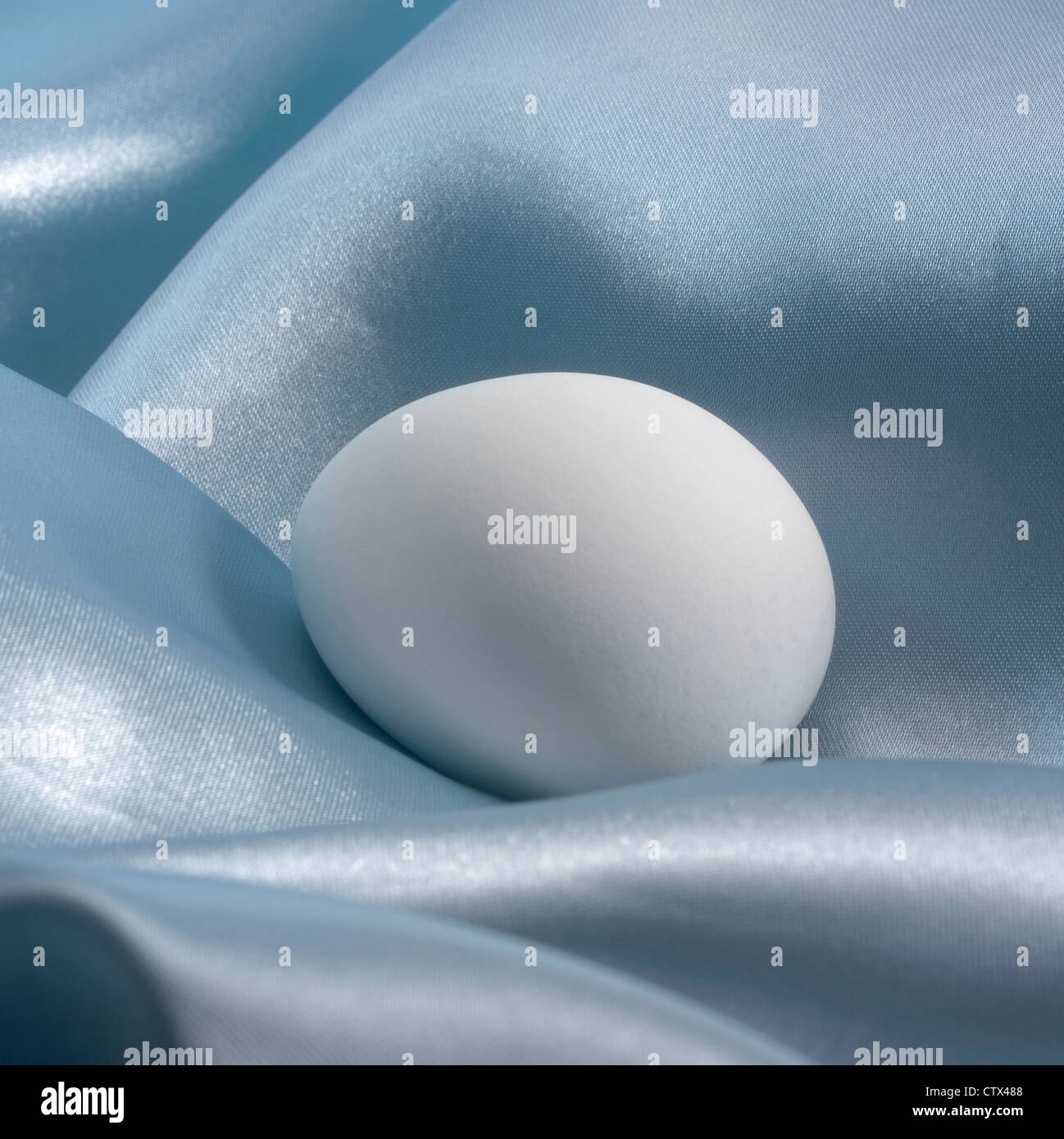 Nobile pasqua tema che mostra un uovo bianco in blu tessuti di raso Foto Stock