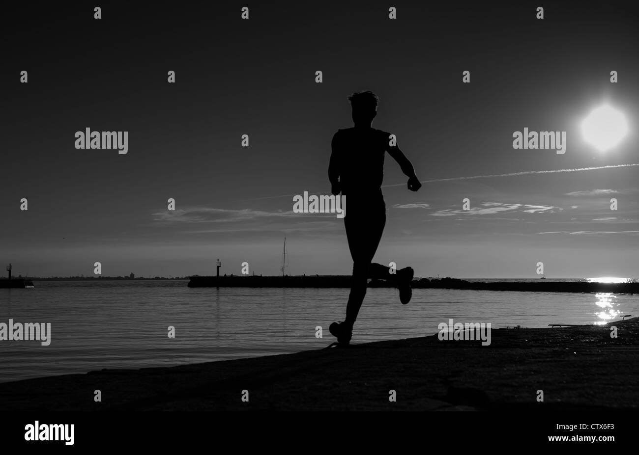 Ombreggiato sportivo a correre lungo la spiaggia sabbiosa di sera tardi Foto Stock