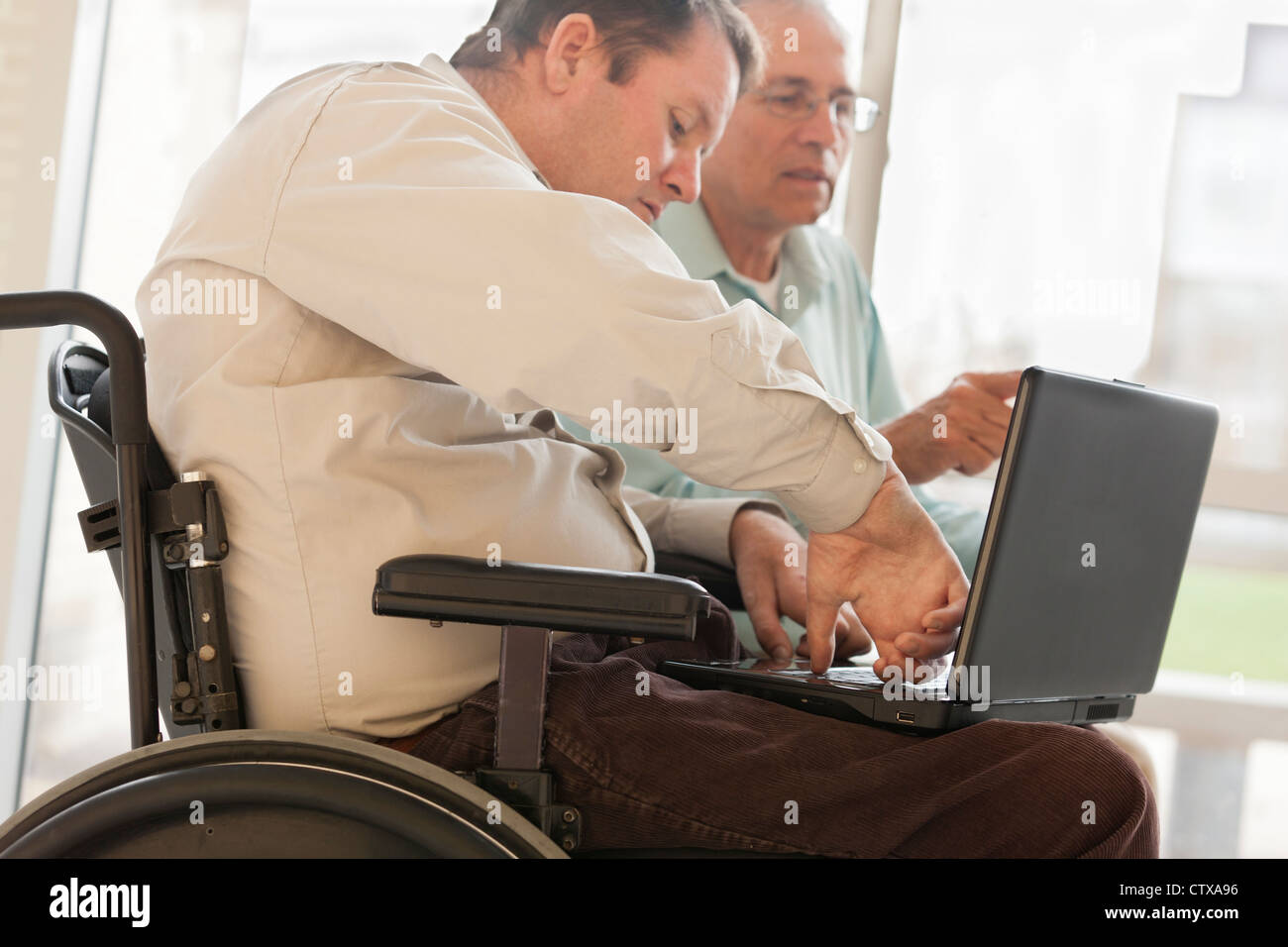 Quadriplegic uomo con lesioni al midollo spinale in sedia utilizzando il pollice per tipo sul computer Foto Stock