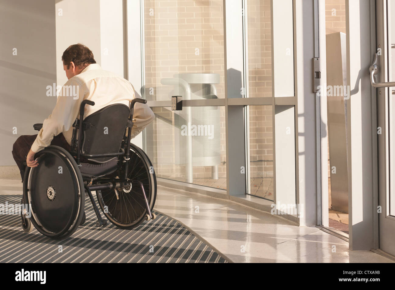 Imprenditore con lesioni al midollo spinale in sedia a rotelle in un edificio per uffici ingresso Foto Stock