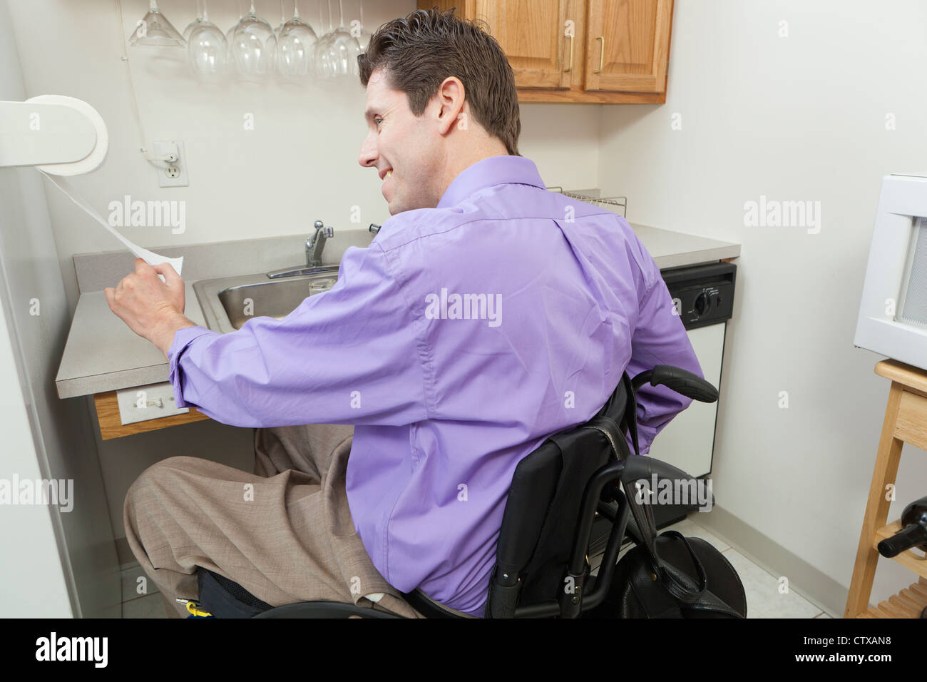 Uomo in carrozzella con lesioni del midollo spinale con un tovagliolo di carta rack in una cucina accessibile Foto Stock