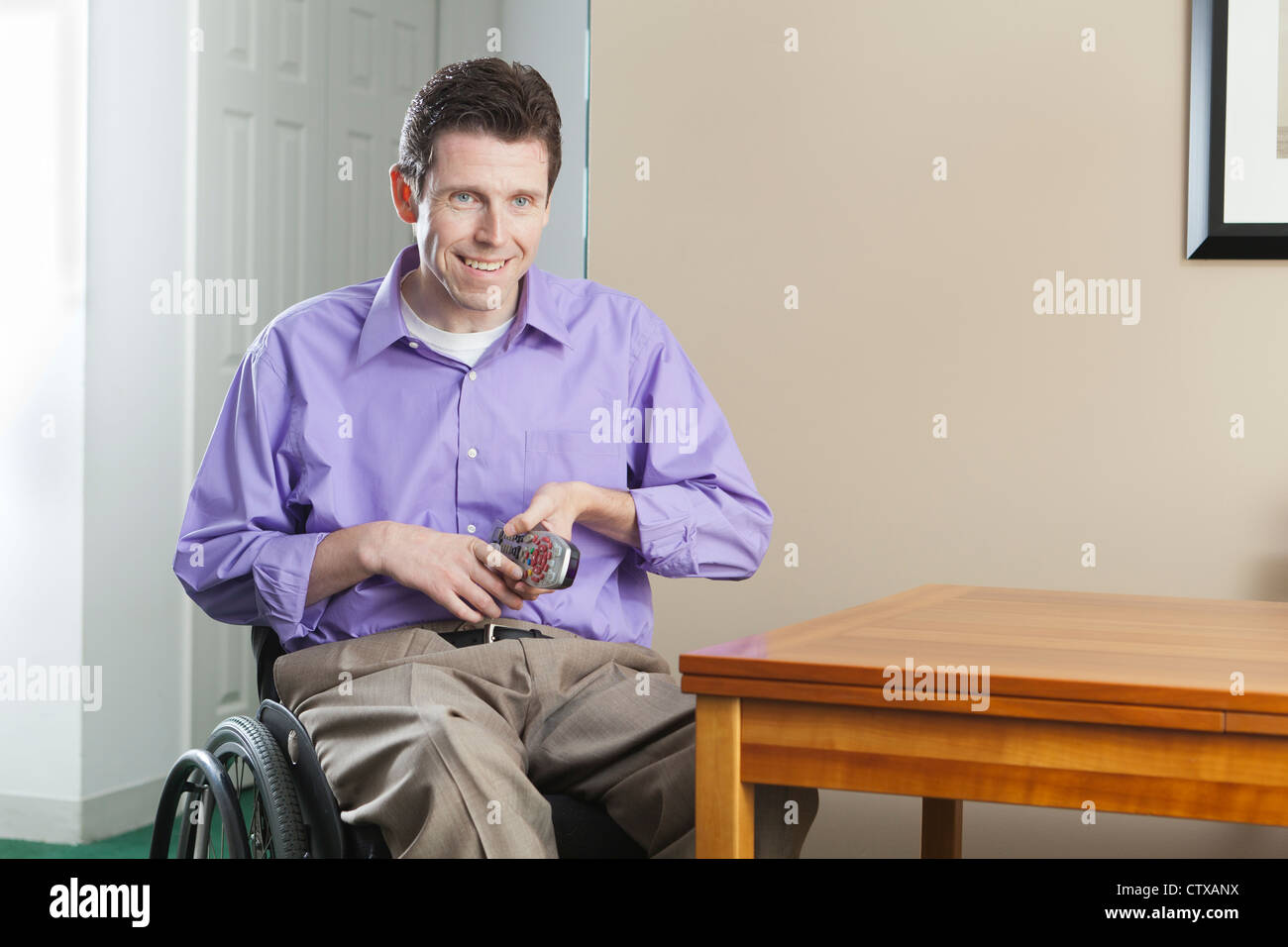 Uomo in carrozzella con lesioni del midollo spinale di prelevare il suo telecomando TV; quadriplegic problema con destrezza manuale Foto Stock