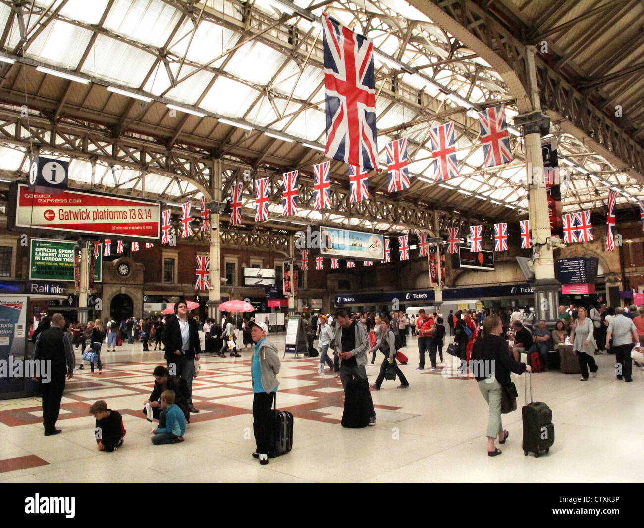 Passeggeri attendere all'interno della stazione ferroviaria di Victoria con Union Jack appesa sopra durante il 2012 Giochi Olimpici ospitati da Londra Foto Stock
