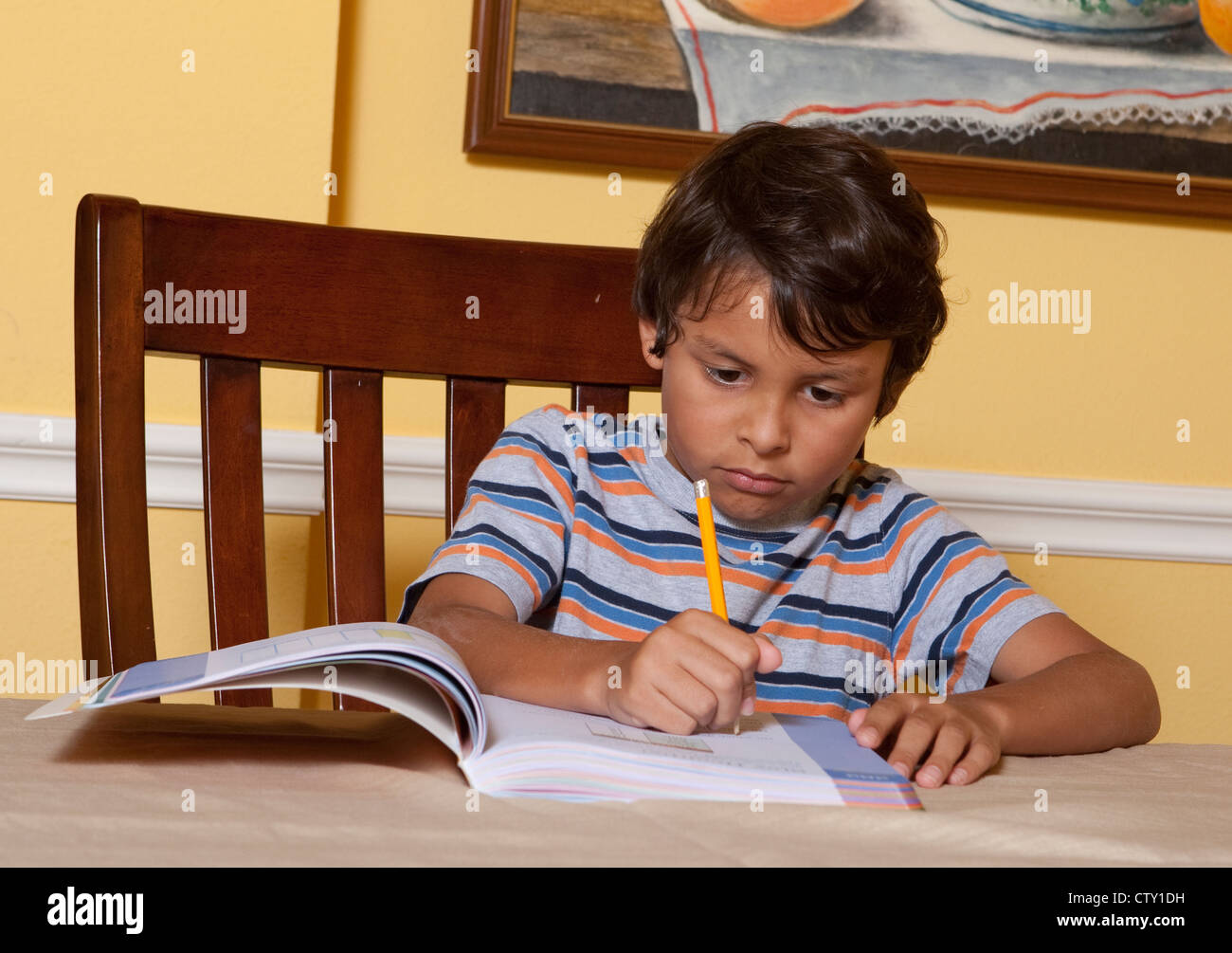 Mexican-American 8 anno vecchia scuola elementare ragazzo di età fa scuola di secondo grado compiti a casa a scrivere, utilizzando una matita Foto Stock