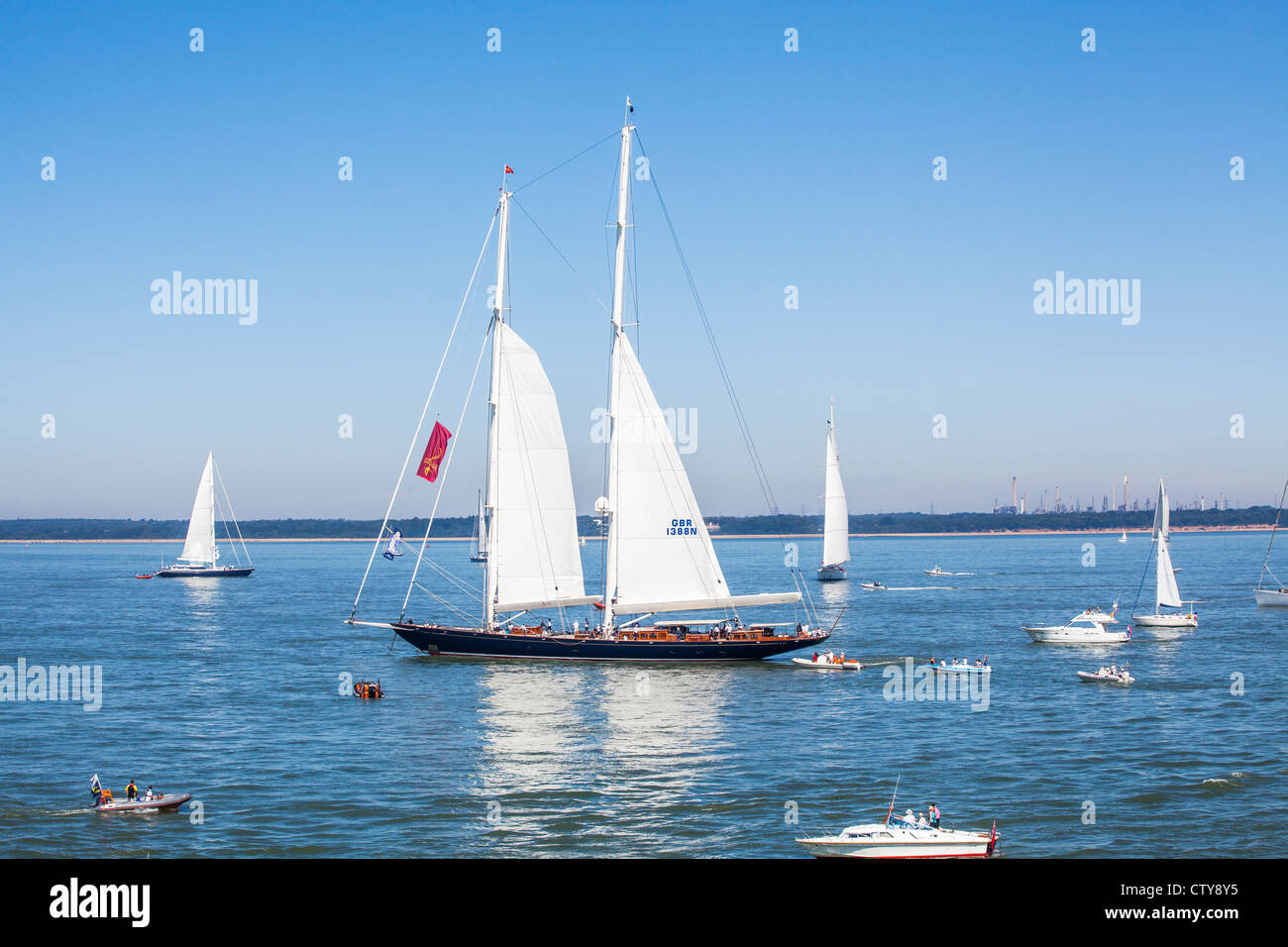 Yacht con due vele prese nel Solent, off Cowes nell'Isola di Wight, in Cowes Week, con una flottiglia di piccole imbarcazioni Foto Stock