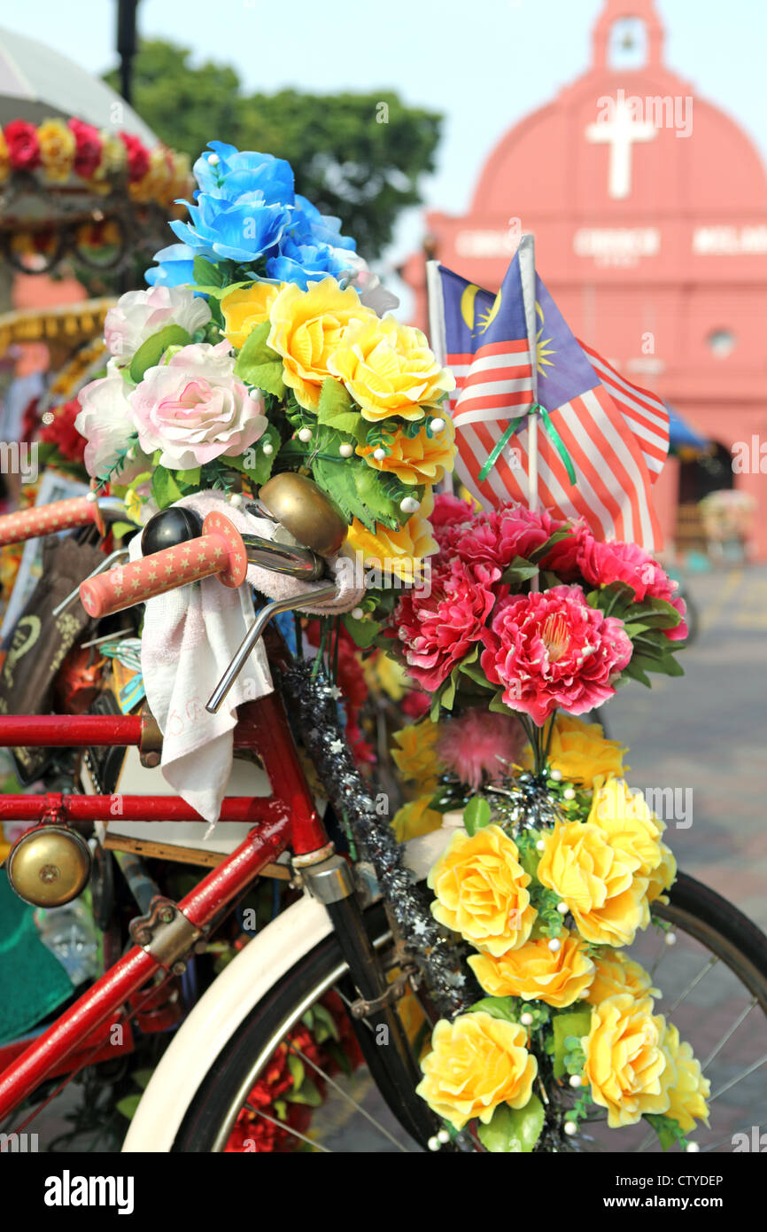 Coloratissimo risciò bicicletta ricoperto di fiori di plastica nella parte anteriore della storica Chiesa di Cristo in Malacca. Foto Stock