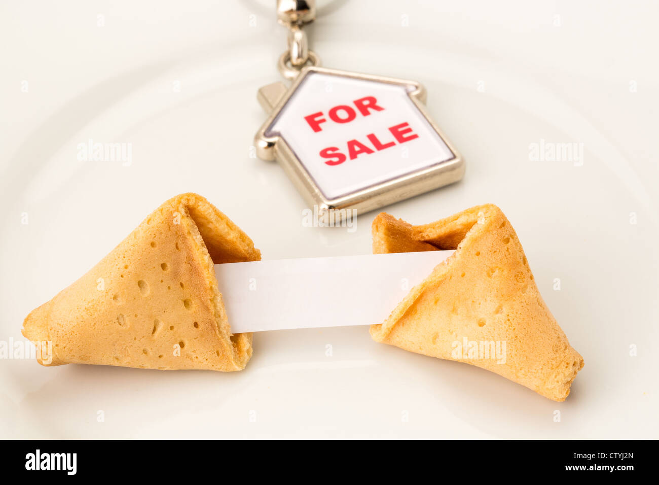 Fortune cookie su una piastra con un messaggio vuoto (pronto per il tuo testo) con una casa in vendita portachiavi, profondità di campo Foto Stock