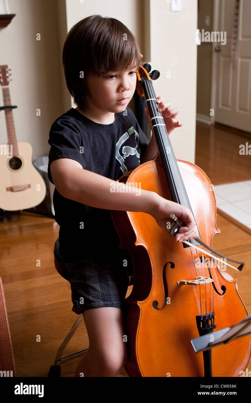 Japanese-American 8 anno vecchio ragazzo pratiche lezioni di musica di violoncello e la lettura di spartiti di musica mentre a casa Foto Stock