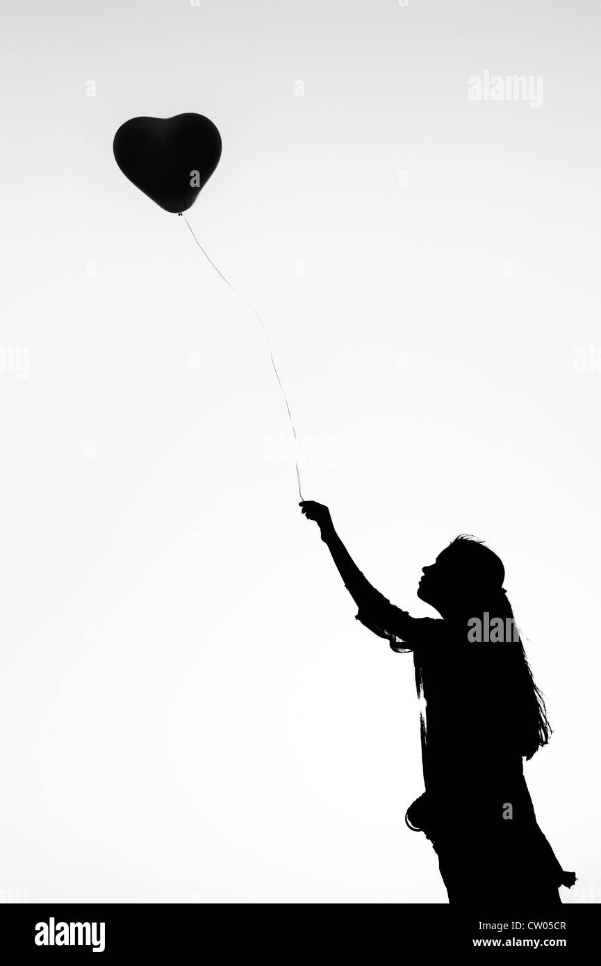 Indian ragazza adolescente tenendo un cuore a forma di palloncino. Silhouette. Monocromatico Foto Stock