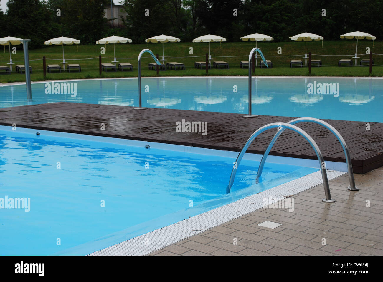 Svuotare una piscina esterna con sedie a sdraio e ombrelloni Foto Stock