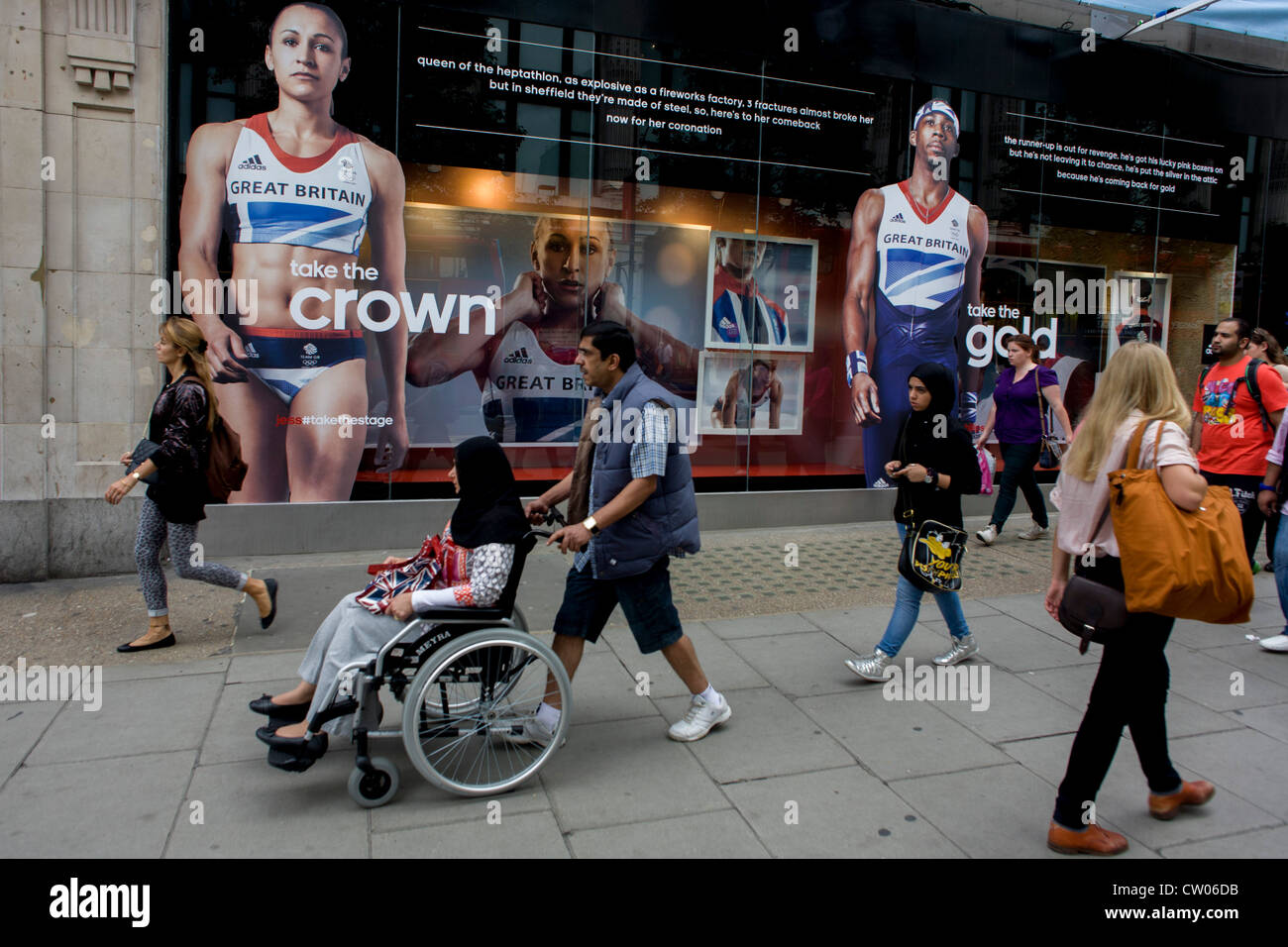 I passanti a piedi sotto le immagini evocative di Team GB gold medallist heptathlete Jessica Ennis e triple ponticello Phillips Idowu adornano l'esterno dell'Adidas store in centro a Londra, in Oxford Street, durante il London 2012 Giochi Olimpici. L'annuncio è per calzature sportive marca Adidas e loro "prendere la fase/corona" campagna che è visualizzabile in tutta la Gran Bretagna e per i britannici che hanno avuto il tifo questi atleti che hanno già vinto medaglie in numeri non visto per 100 anni. Foto Stock