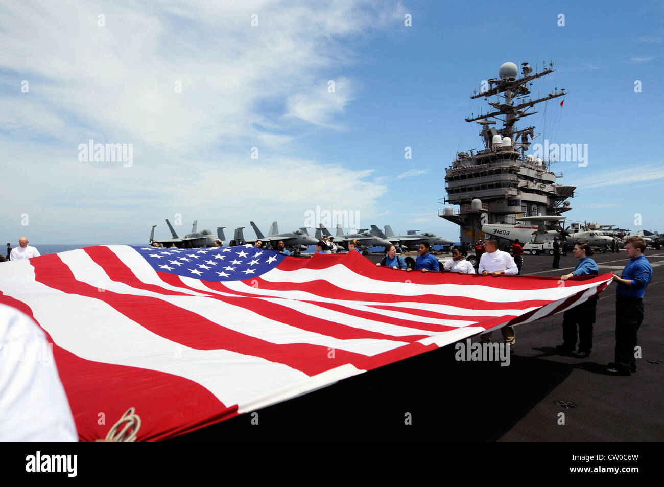 I marinai tengono in mano l'insegna nazionale sul ponte di volo della portaerei di classe Nimitz USS Abraham Lincoln (CVN 72) durante una dimostrazione di potenza aerea. Lincoln è in viaggio verso gli Stati Uniti per completare un cambio di homeport di otto mesi durante il quale operava nelle aree di responsabilità della flotta degli Stati Uniti 5, 6 e 7. Foto Stock