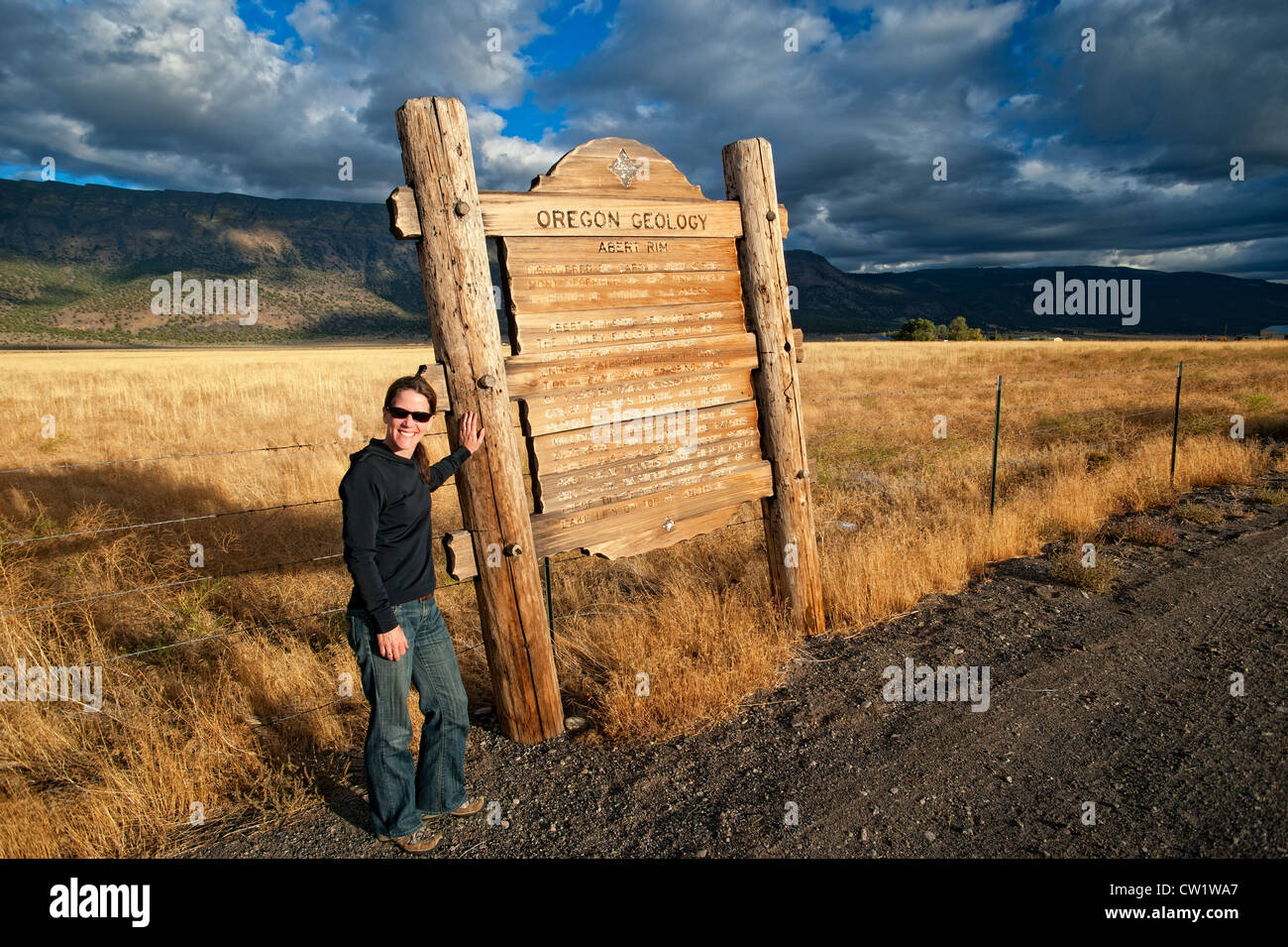 Donna in piedi presso la Oregon Geologia informazioni stradali segno che descrive una anomalia geologica line chiamato Abert Rim, visibile in foto dello sfondo. Stati Uniti d'America Foto Stock