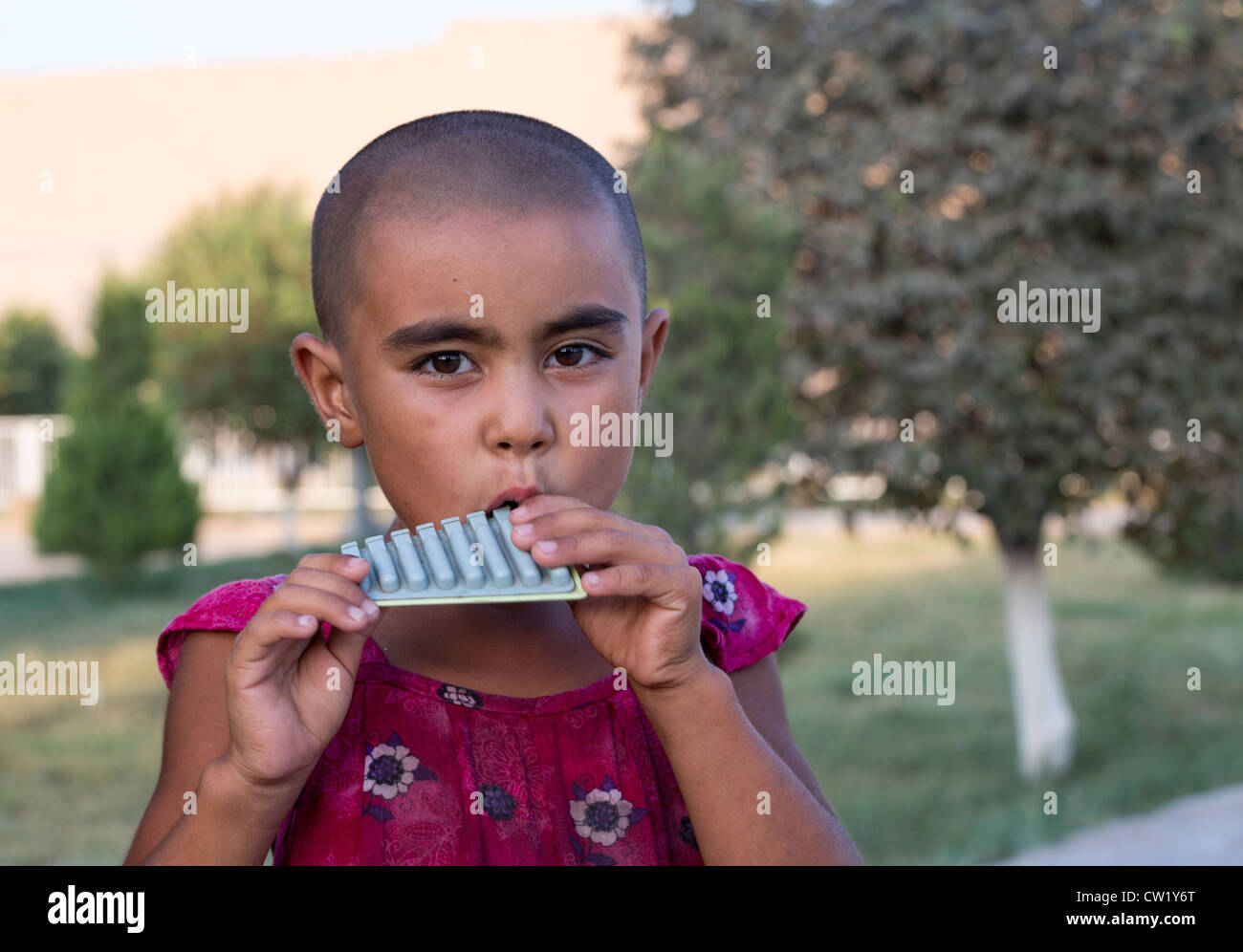 Ragazza giovane con la testa rasata giocando pan tubazioni, Khiva, Uzbekistan Foto Stock