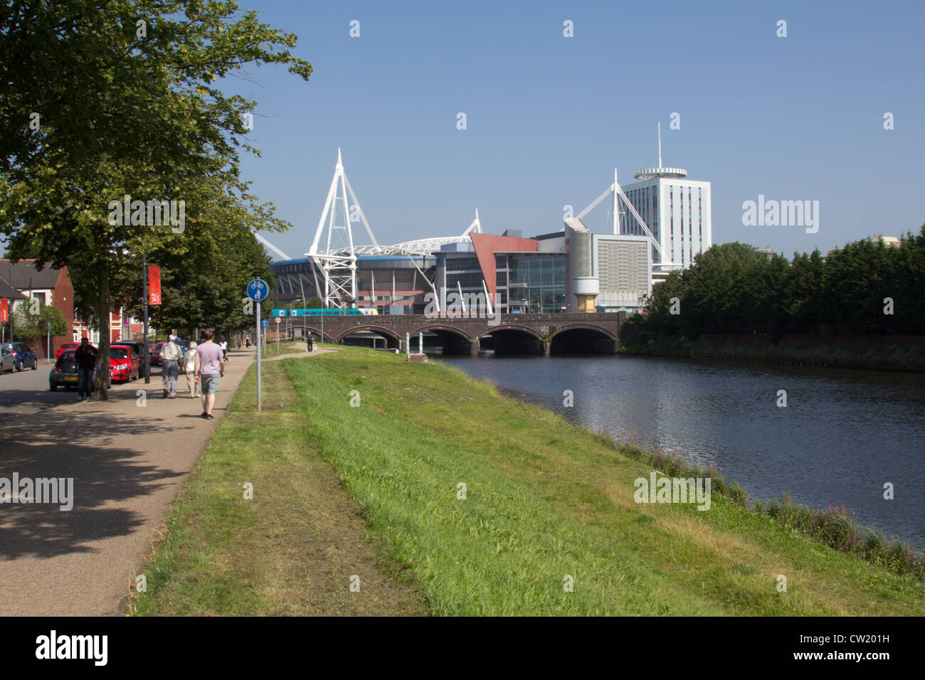 I camminatori potrete crogiolarvi al sole lungo Taffs Mead sulle rive del fiume con Cardiff Millennium Stadium a distanza Foto Stock