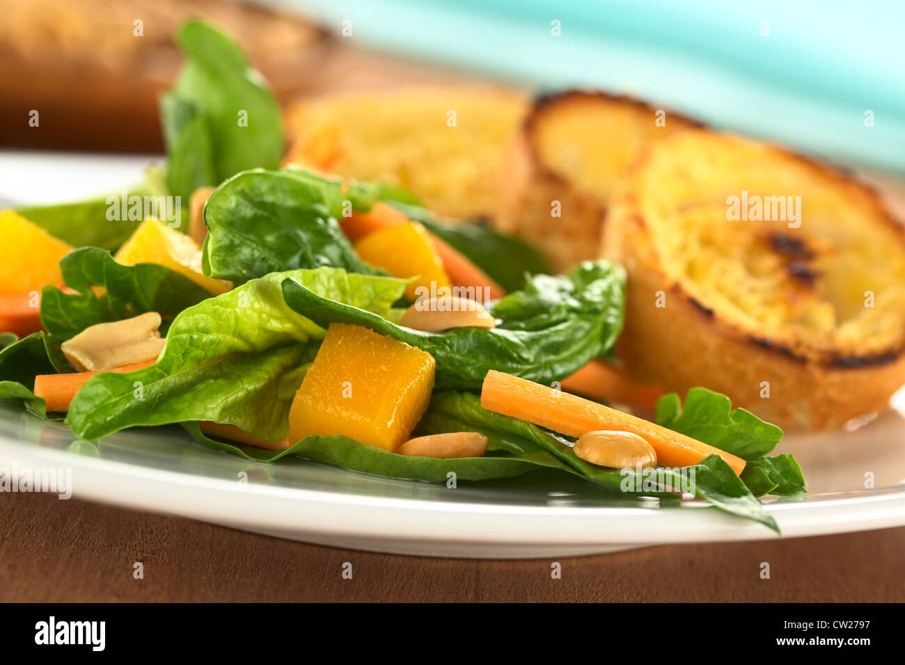 Spinaci freschi, mango e insalata di carote con arachidi sulla sommità e fritto baguette fette in retro Foto Stock