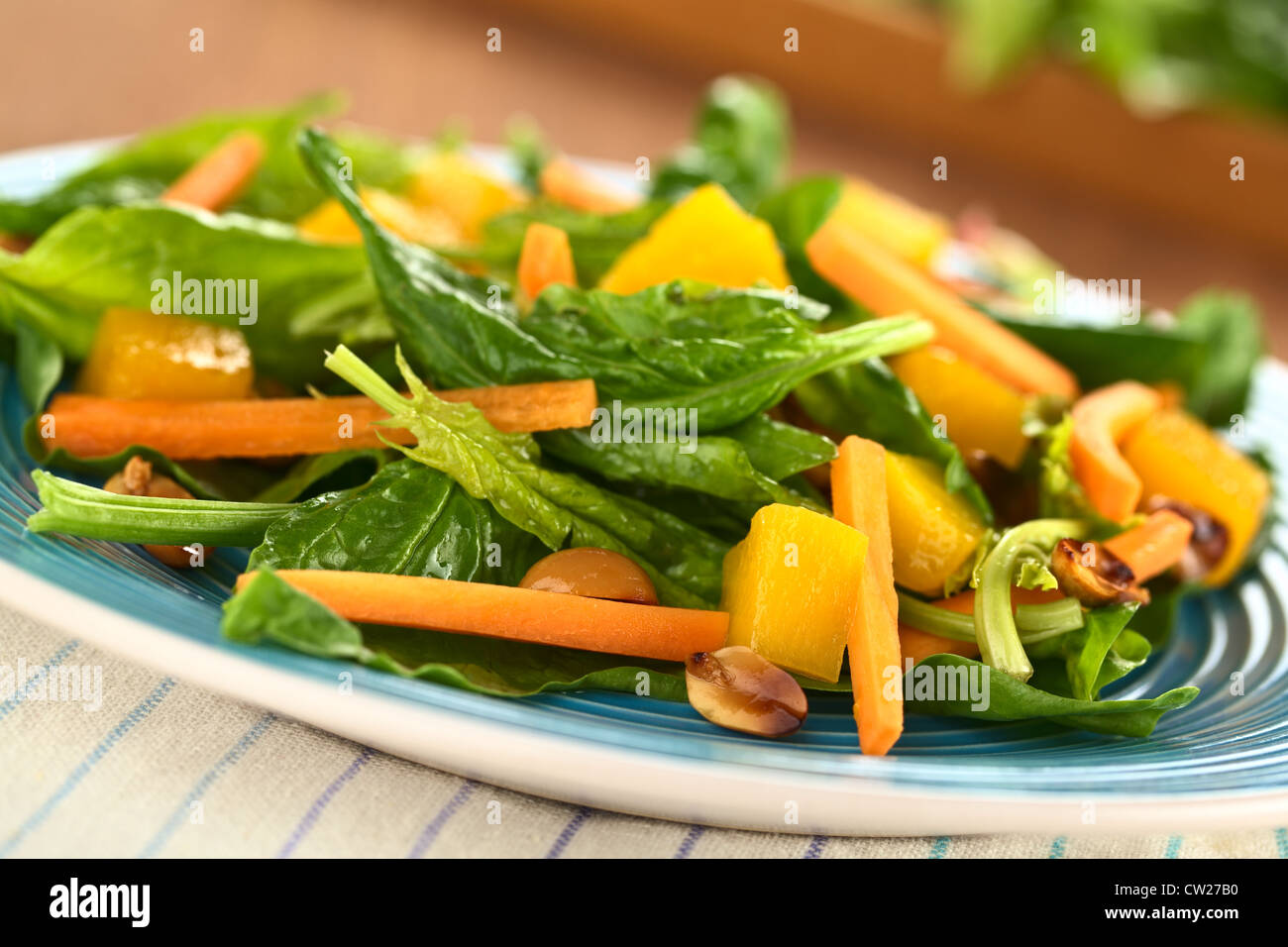 Spinaci freschi, mango e insalata di carote con arachidi sulla piastra blu (messa a fuoco selettiva, concentrarsi sul pezzo di mango nella parte anteriore) Foto Stock