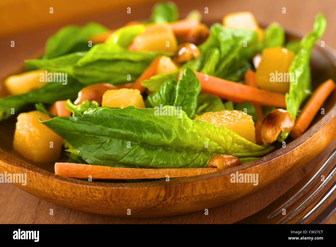 Spinaci freschi, mango e insalata di carote con arachidi sul piatto di legno con forca Foto Stock