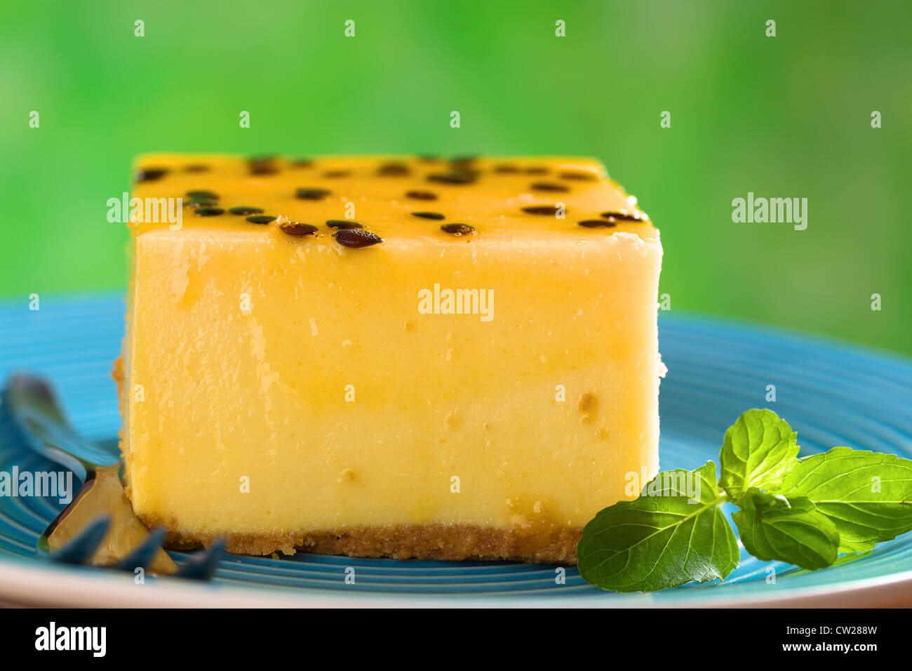 Freschi frutti della passione cheesecake dessert su piastra blu con foglia di menta e forcella di pasticceria Foto Stock