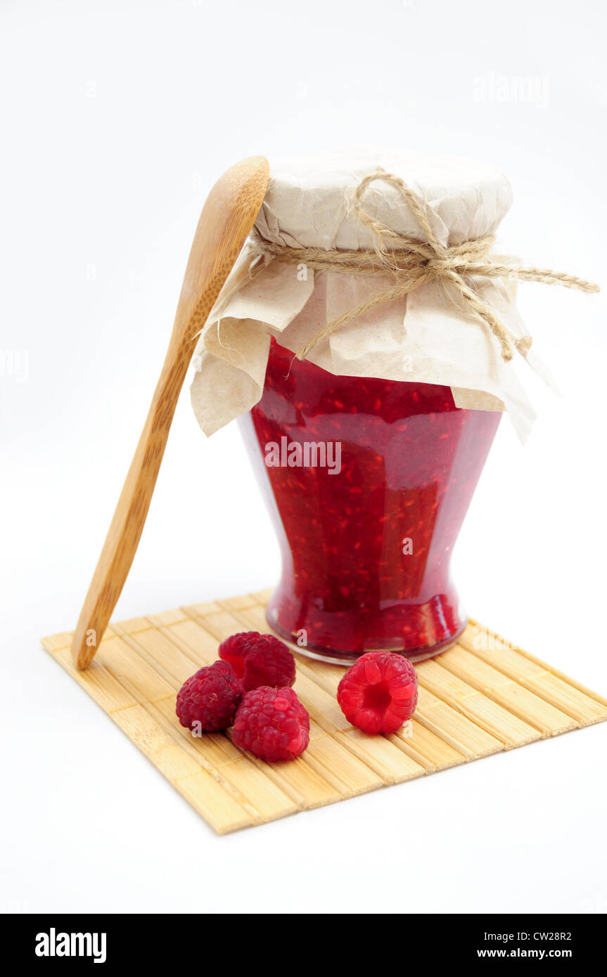 Un vasetto di marmellata di lamponi con frutta fresca con il cucchiaio di legno sulle montagne russe in legno Foto Stock