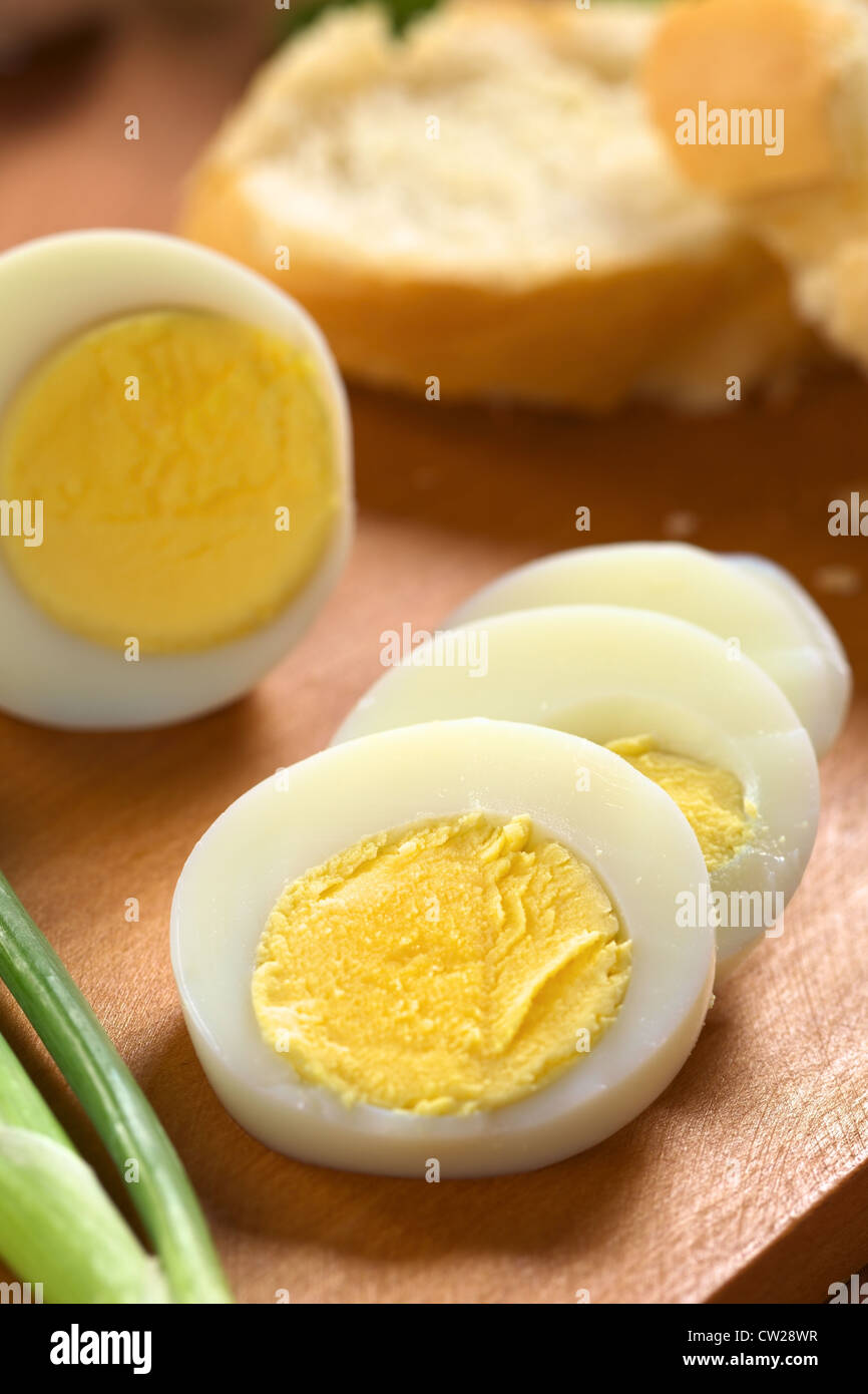 Fresh uovo sodo tagliato a fette con lo scalogno accanto e baguette nella parte posteriore sul tagliere di legno Foto Stock