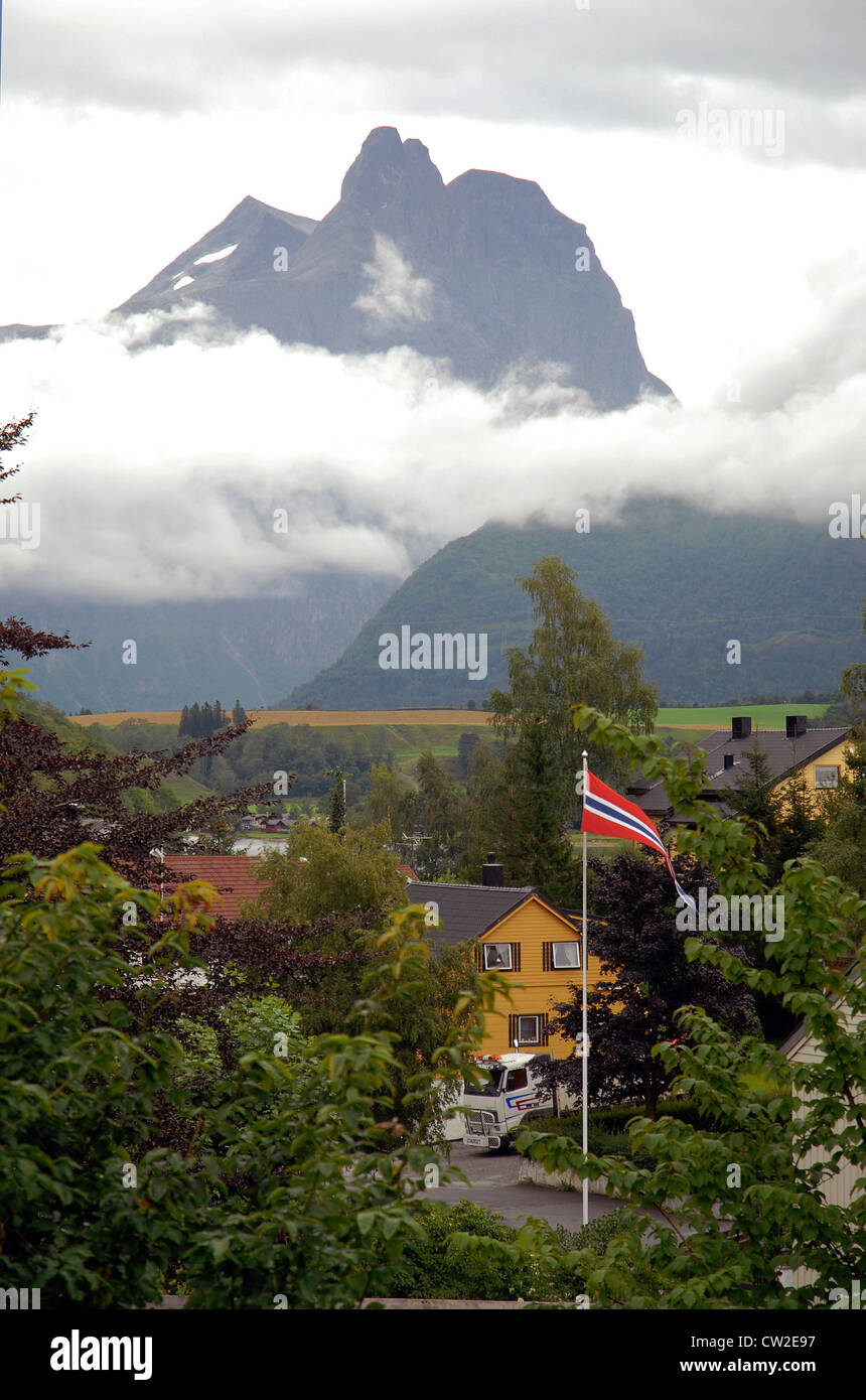 Romsdalhorn sopra le nuvole, Romsdal Valley, Fjordland, Norvegia, case in legno e bandiera norvegese Foto Stock