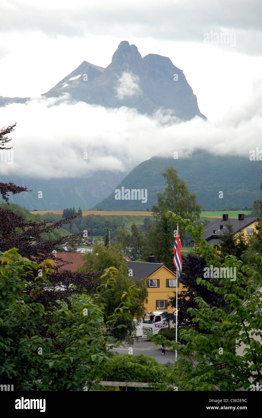 Romsdalhorn sopra le nuvole, Romsdal Valley, Fjordland, Norvegia, case in legno e bandiera norvegese Foto Stock