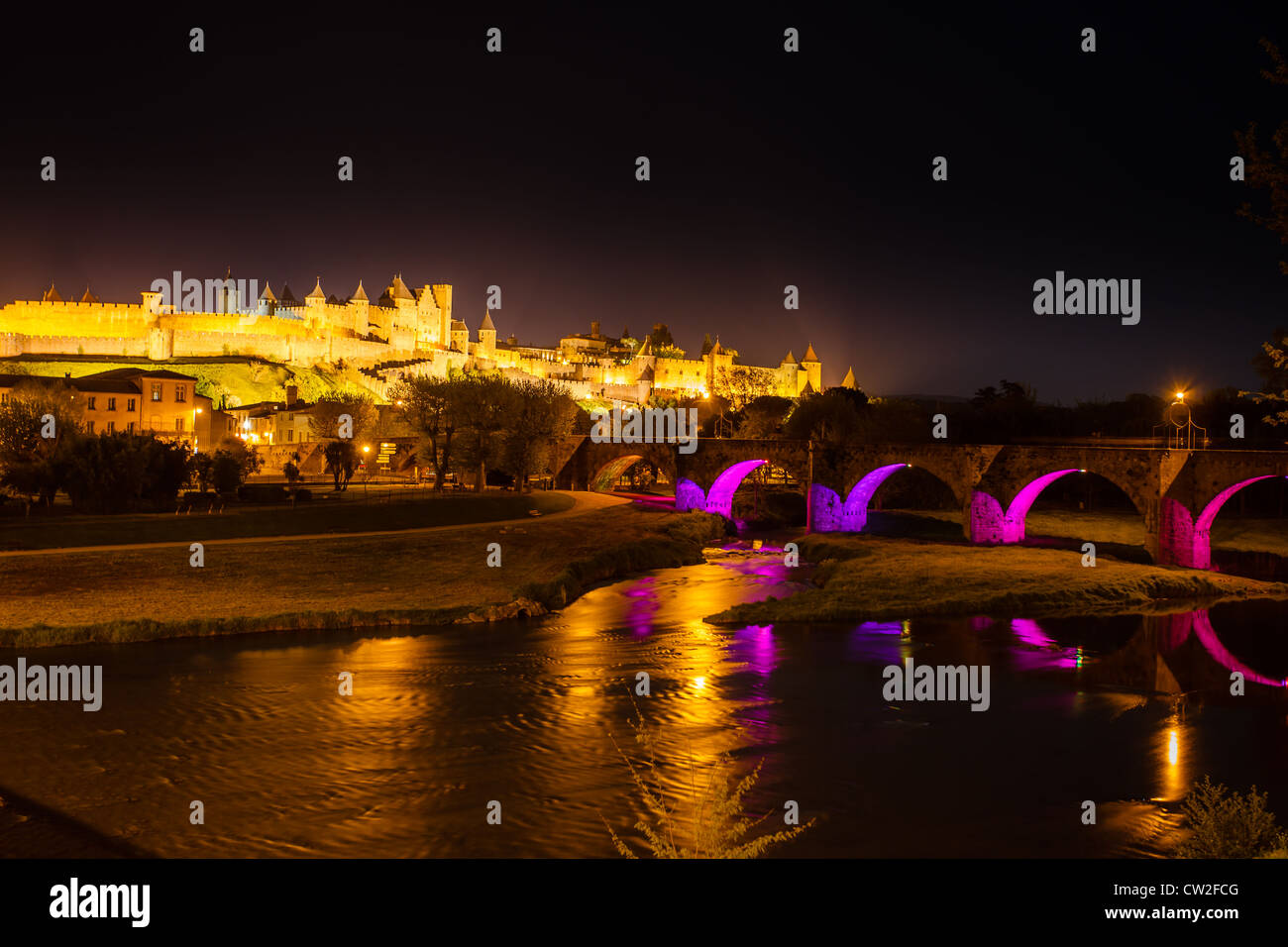 Illuminata bastioni medievali di antica città fortificata di Carcassonne con rosa luminoso viola gli archi del Ponte in nero cielo notturno Foto Stock