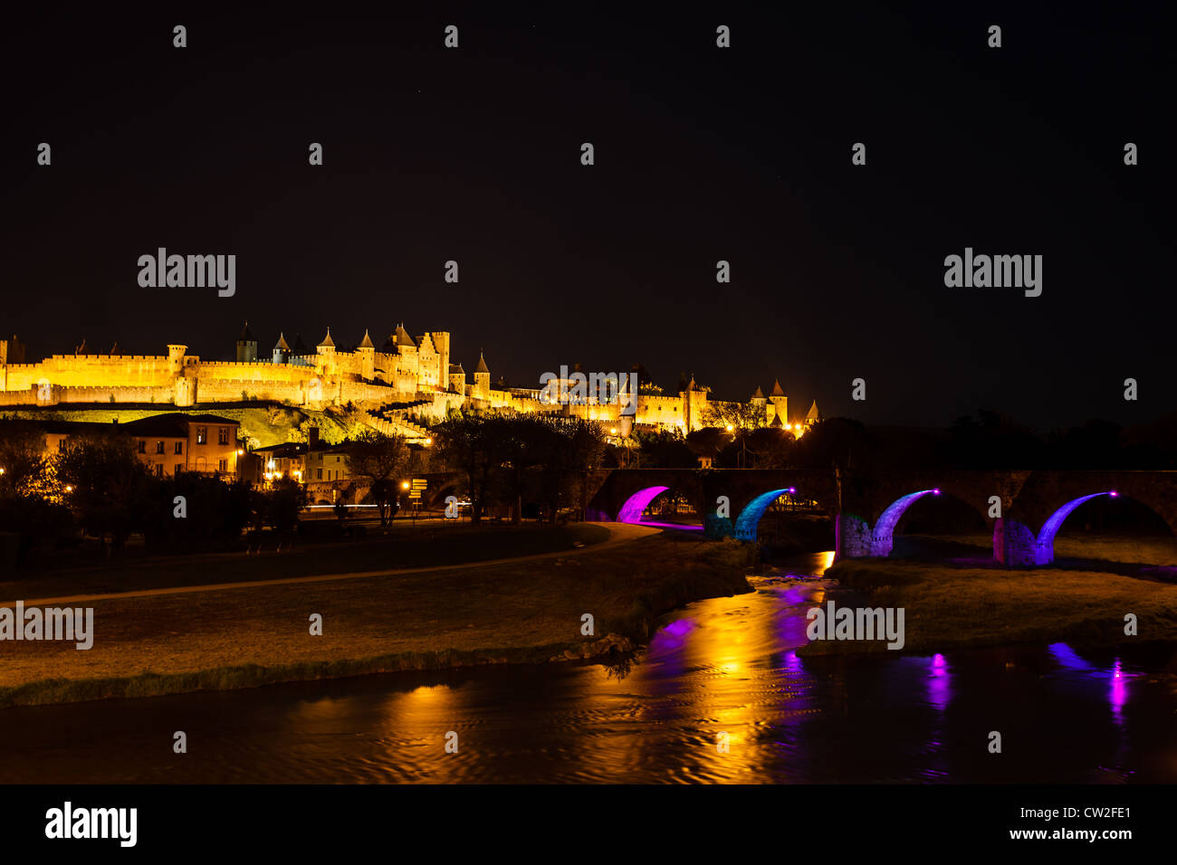 Luminosa di bastioni medievali di antica città fortificata di Carcassonne con rosa illuminato blu archi del Ponte in nero cielo notturno. Foto Stock