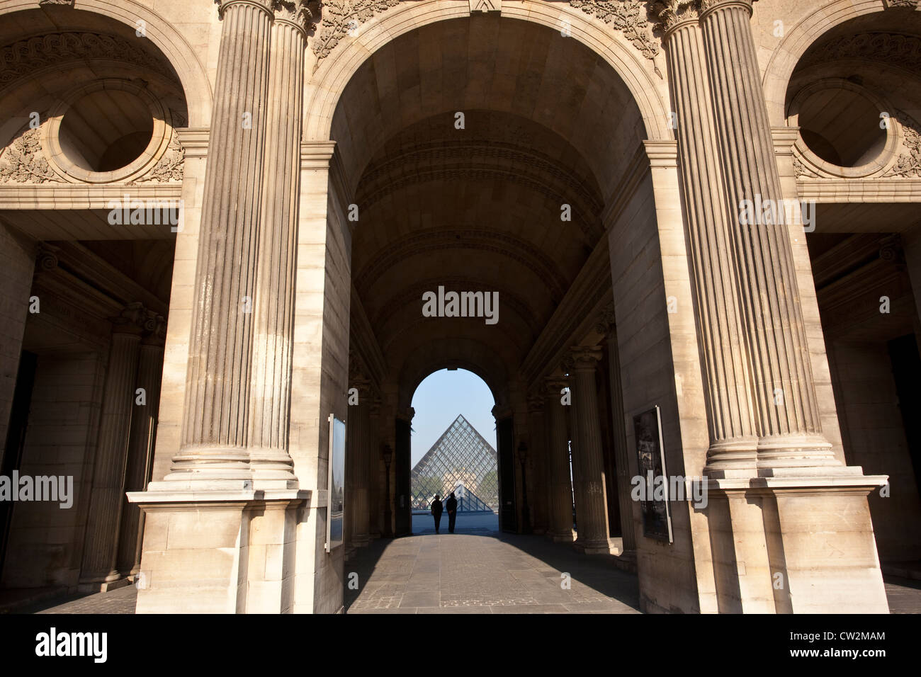 Un giovane a piedi attraverso il Palais du Louvre verso la piramide di vetro al Musée du Louvre, Paris, Francia. Foto Stock