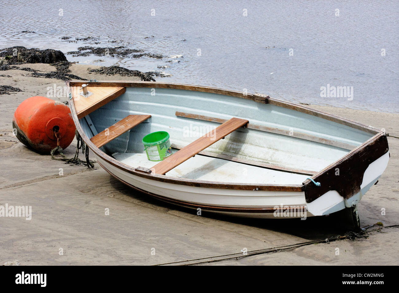 Una piccola barca a remi spiaggiata sulla linea di marea. Foto Stock