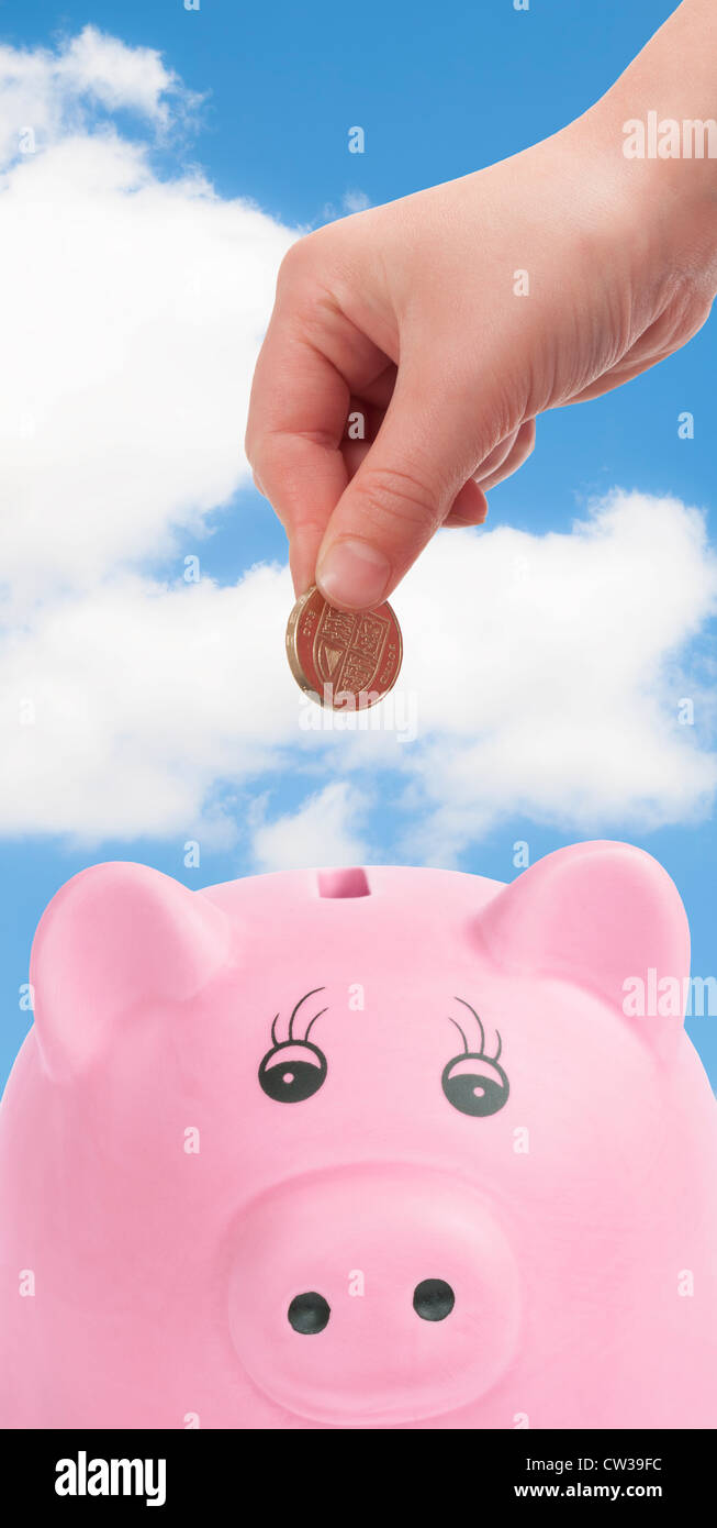 Maiale rosa scatola di denaro con la mano la deposizione di British pound coin Foto Stock