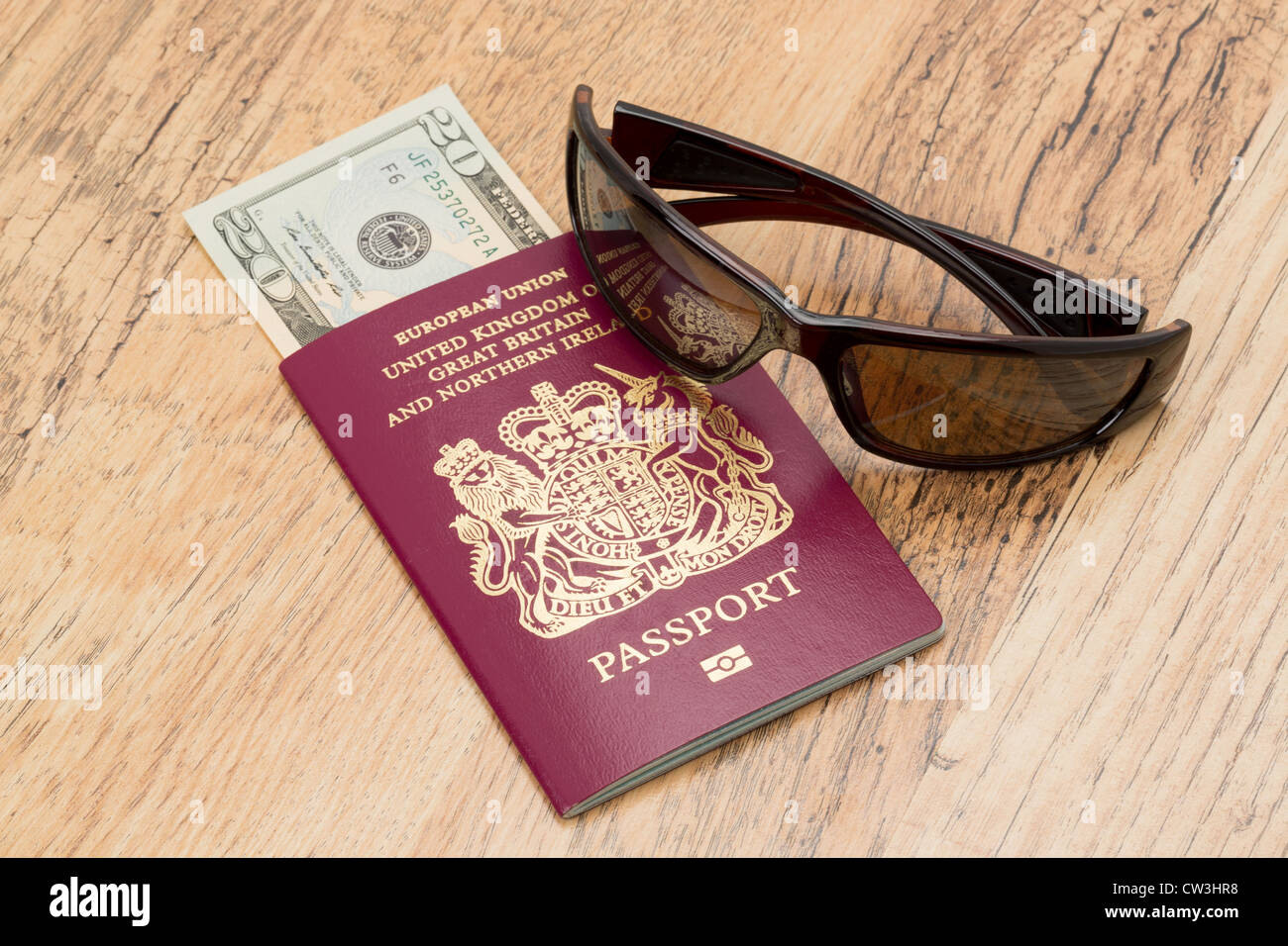 Un passaporto del Regno Unito con un 20 US Dollar nota e raffreddare gli occhiali da sole collocato su un tavolo - temi di viaggio Foto Stock