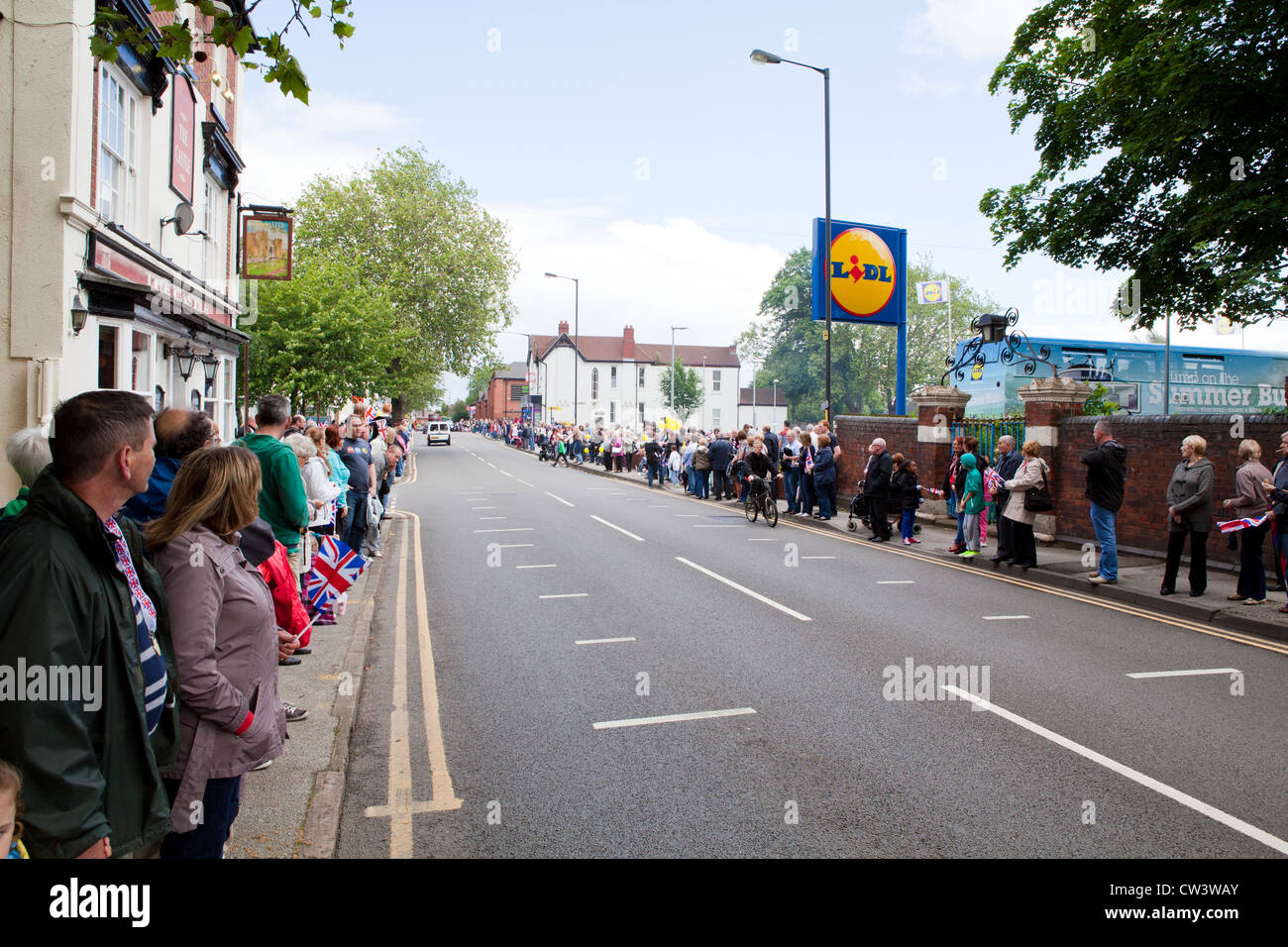 La folla line New Road, Willenhall, West Midlands per attendere il passaggio della torcia Olimpica e il suo portatore Foto Stock