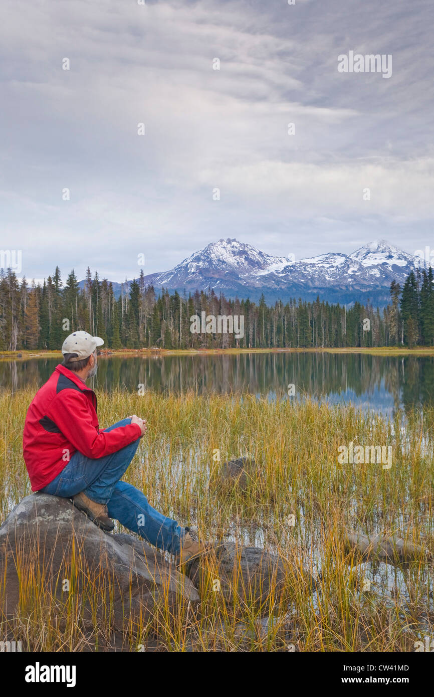 Uomo seduto su di una roccia a lago, lago di Scott, le tre sorelle, Willamette National Forest, Oregon, Stati Uniti d'America Foto Stock