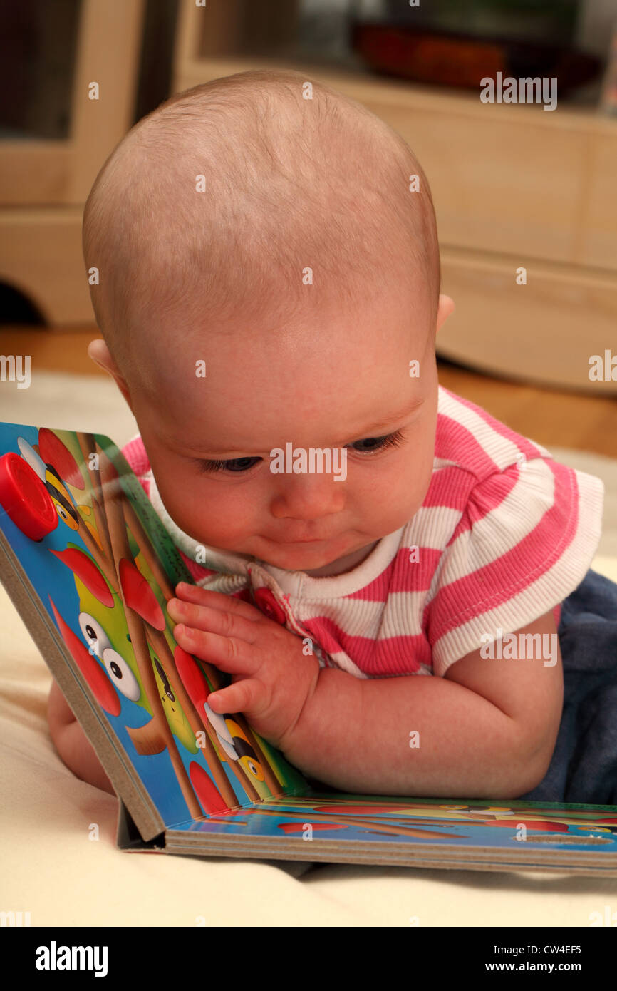 A sei mesi bambina guarda facinated dai colori di un libro di fotografia Foto Stock