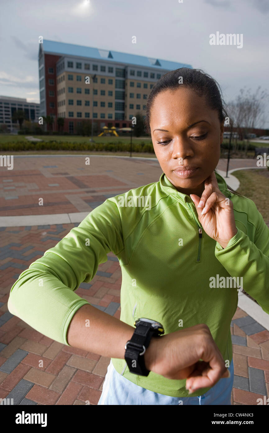 Giovane donna in abbigliamento sportivo cercando il suo orologio con edificio in background Foto Stock