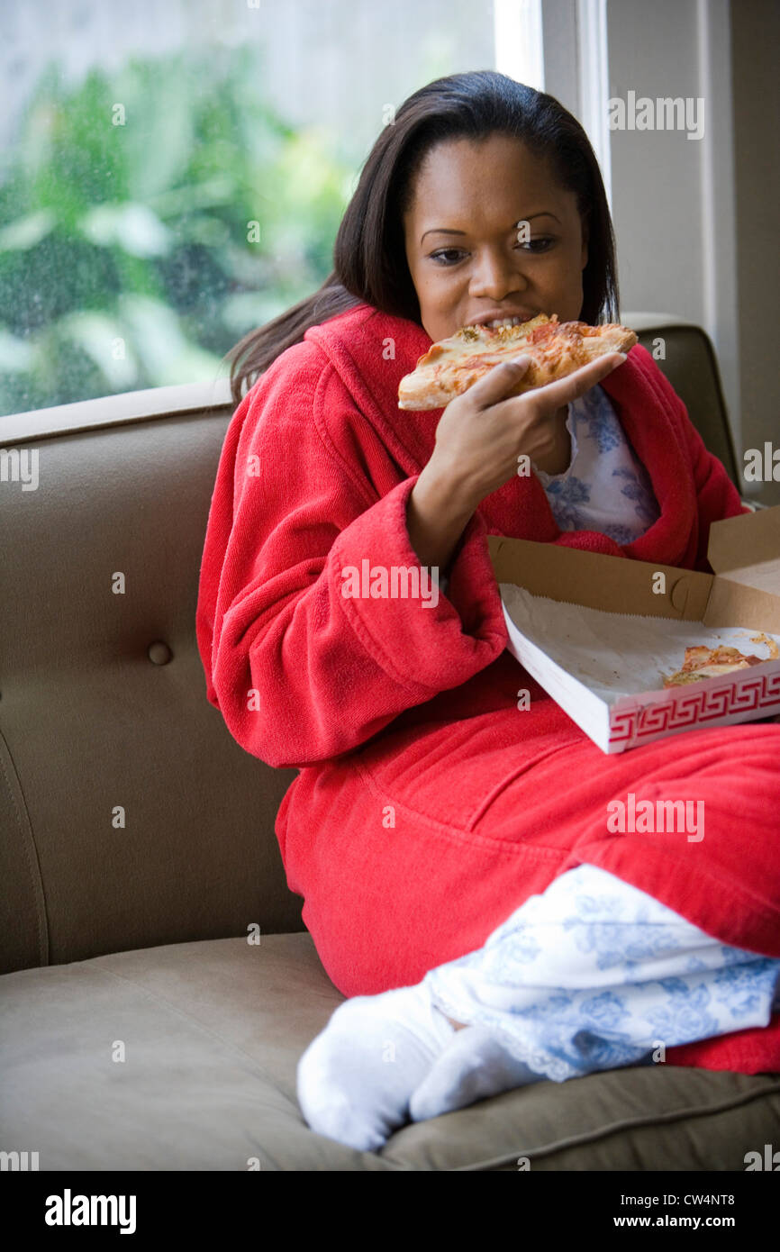 Giovane donna in abito di mangiare la pizza su un divano Foto Stock