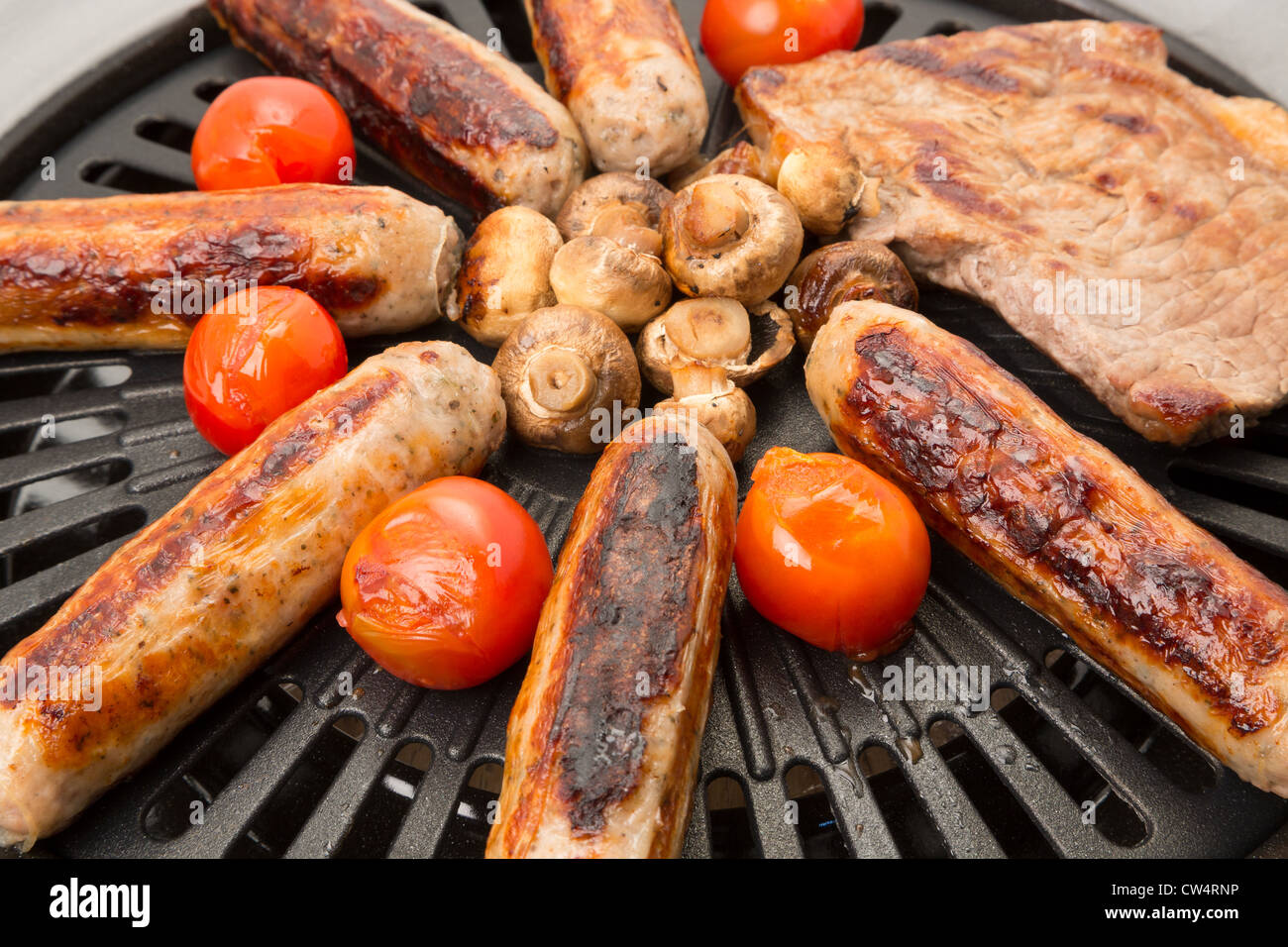 Salsicce e la bistecca sul barbecue con alcuni pomodori e funghi Foto Stock