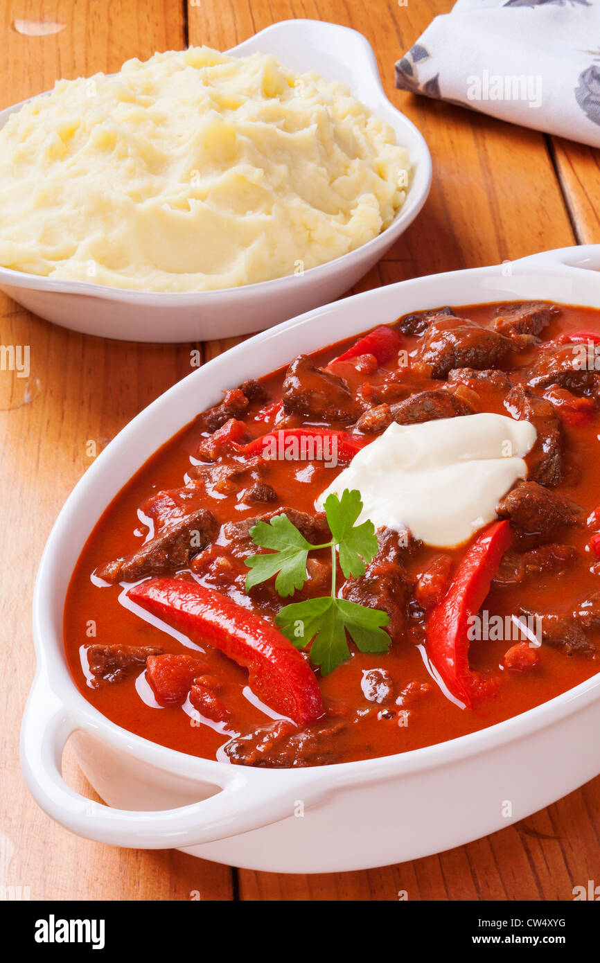 Gulasch con peperoni rossi e panna acida e un piatto di lato di purea di patata. Foto Stock