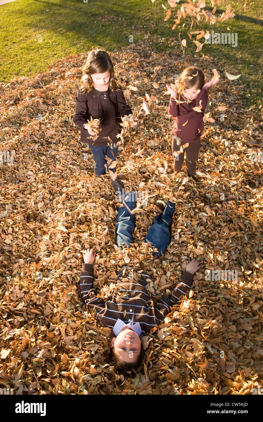 Bambini che giocano su un mucchio di foglie secche in un parco Foto Stock