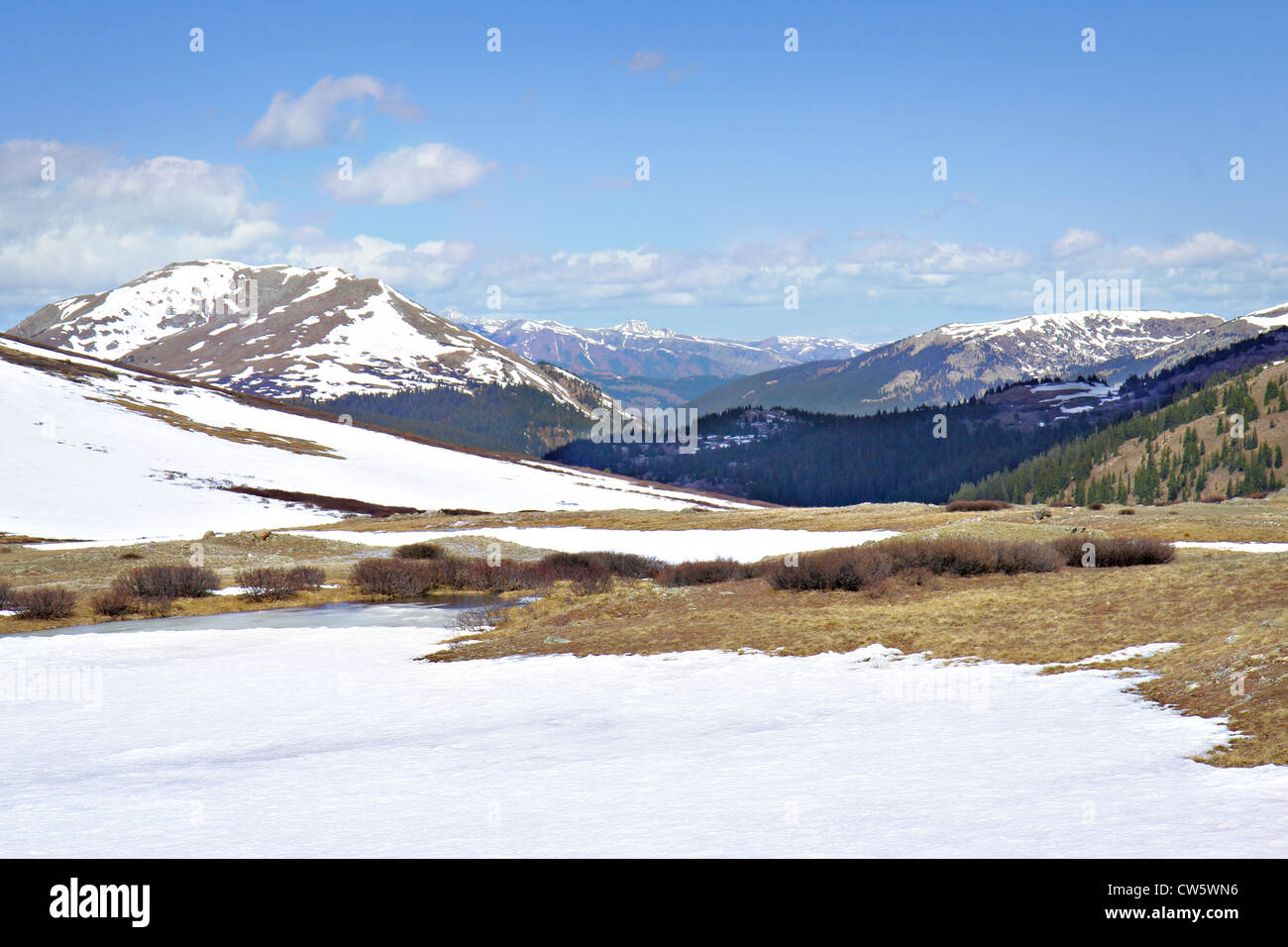 Tundra alpina parzialmente coperto dalla neve con cime innevate rientranti nella sfondo sotto parzialmente nuvoloso blu del cielo Foto Stock